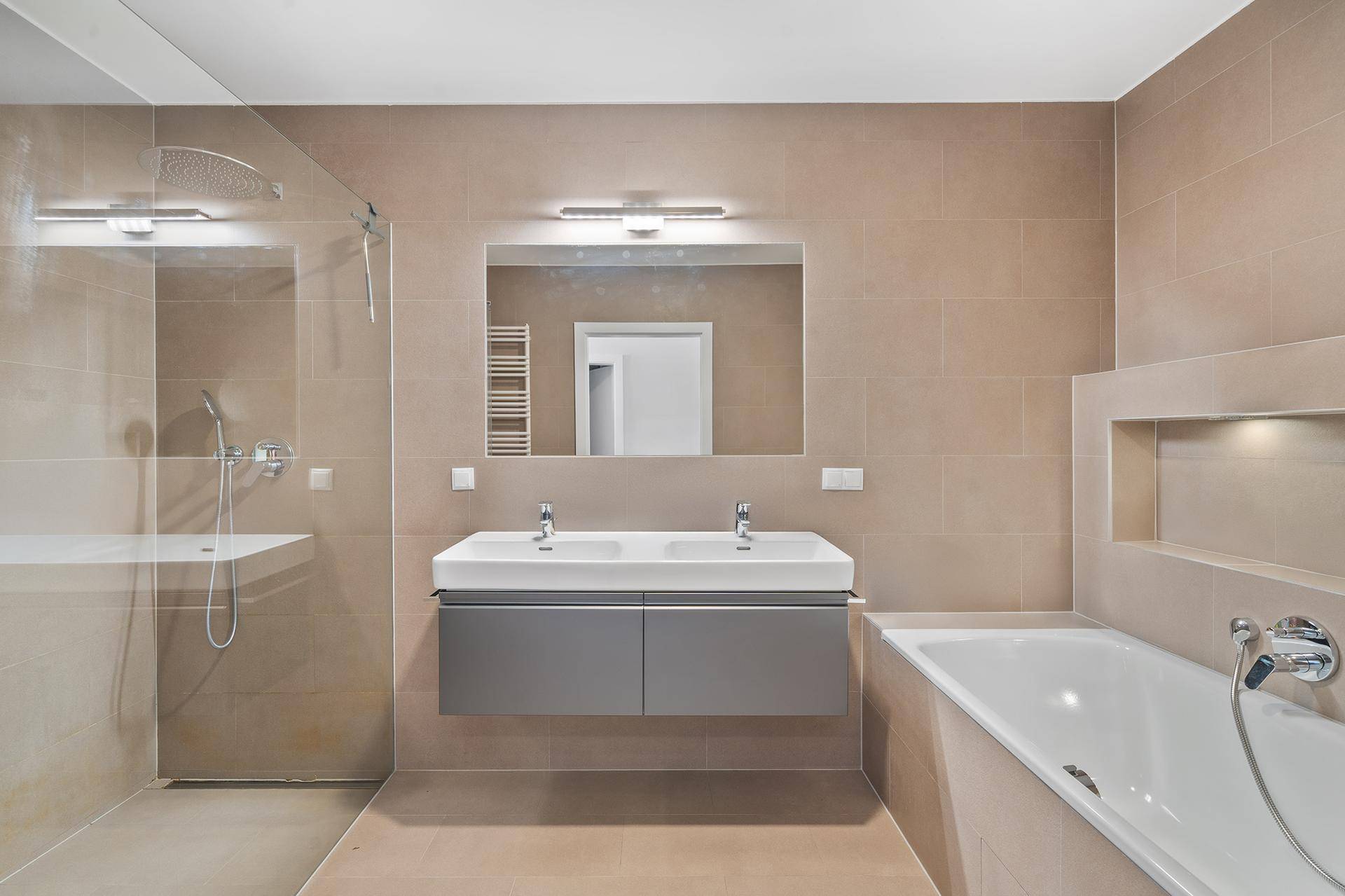 Modernes Badezimmer mit Doppelwaschbecken, großer Dusche und Badewanne in hellen Fliesen.