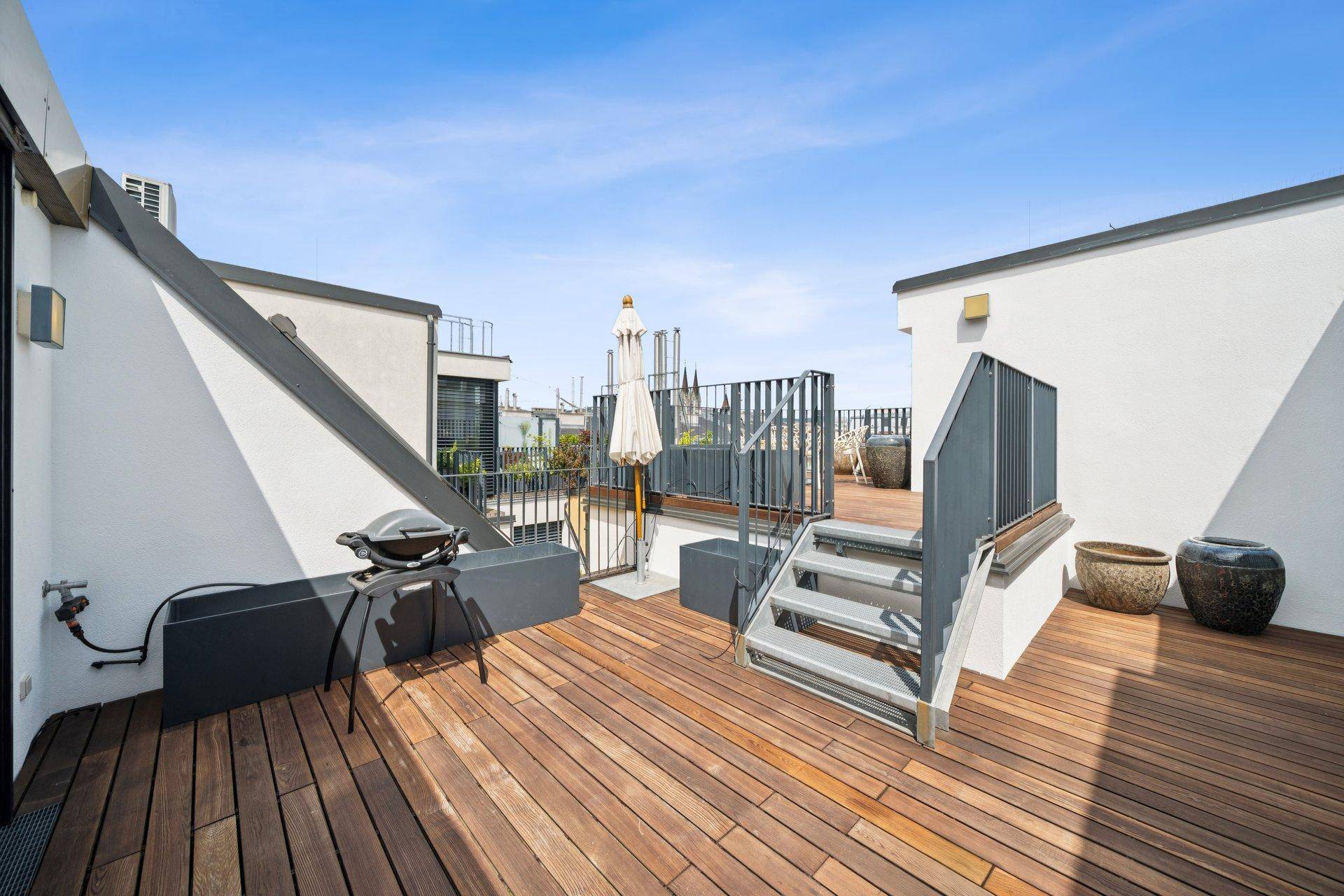 Geräumige Dachterrasse mit Holzdeck, Grillbereich und Treppe zu weiteren Ebenen.