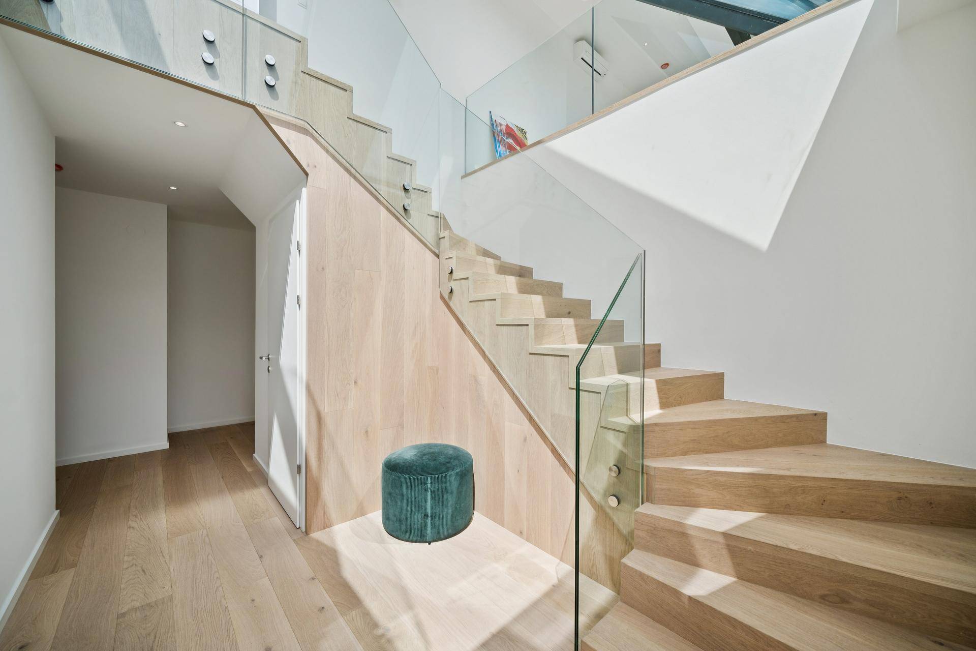 Elegantes Treppenhaus mit Holzstufen und Glasgeländer, das die verschiedenen Ebenen verbindet.