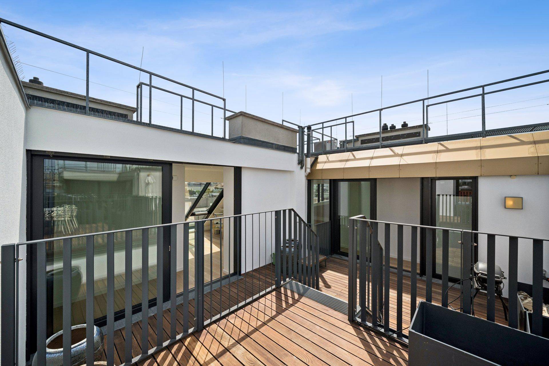 Dachterrasse mit Holzdeck und Metallgeländer, die Zugang zu weiteren Außenbereichen bietet.