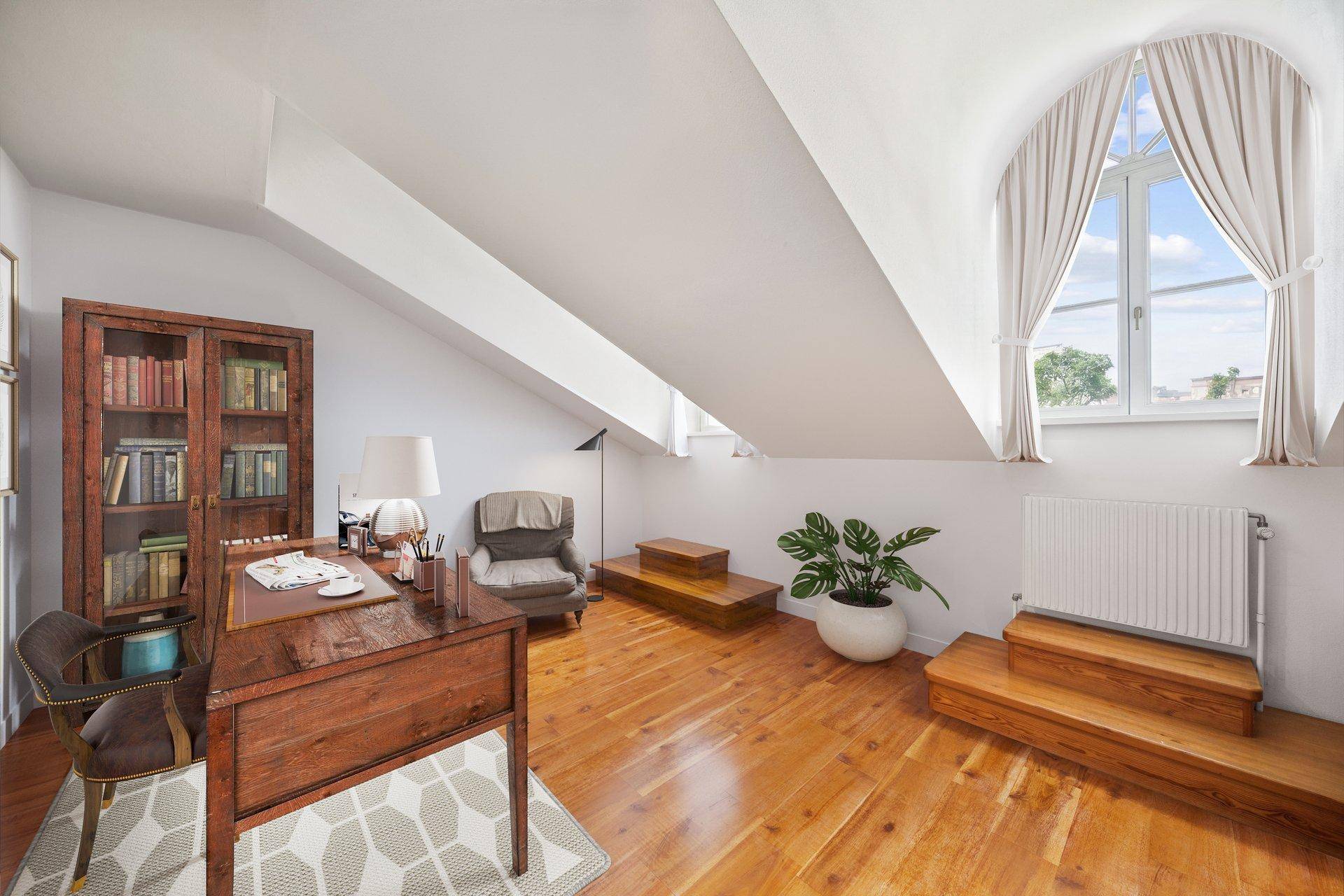 Helles Arbeitszimmer im Dachgeschoss mit Holzboden, schrägen Wänden und einem Rundbogenfenster.
