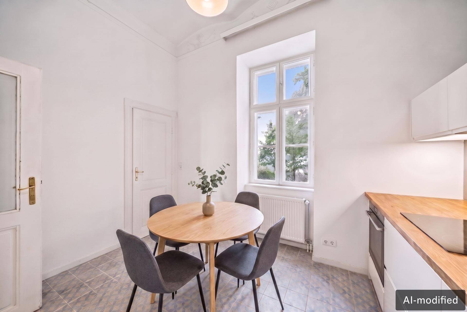 Helle Wohnküche mit Esstisch, Fliesenboden und Blick ins Grüne durch das große Fenster.