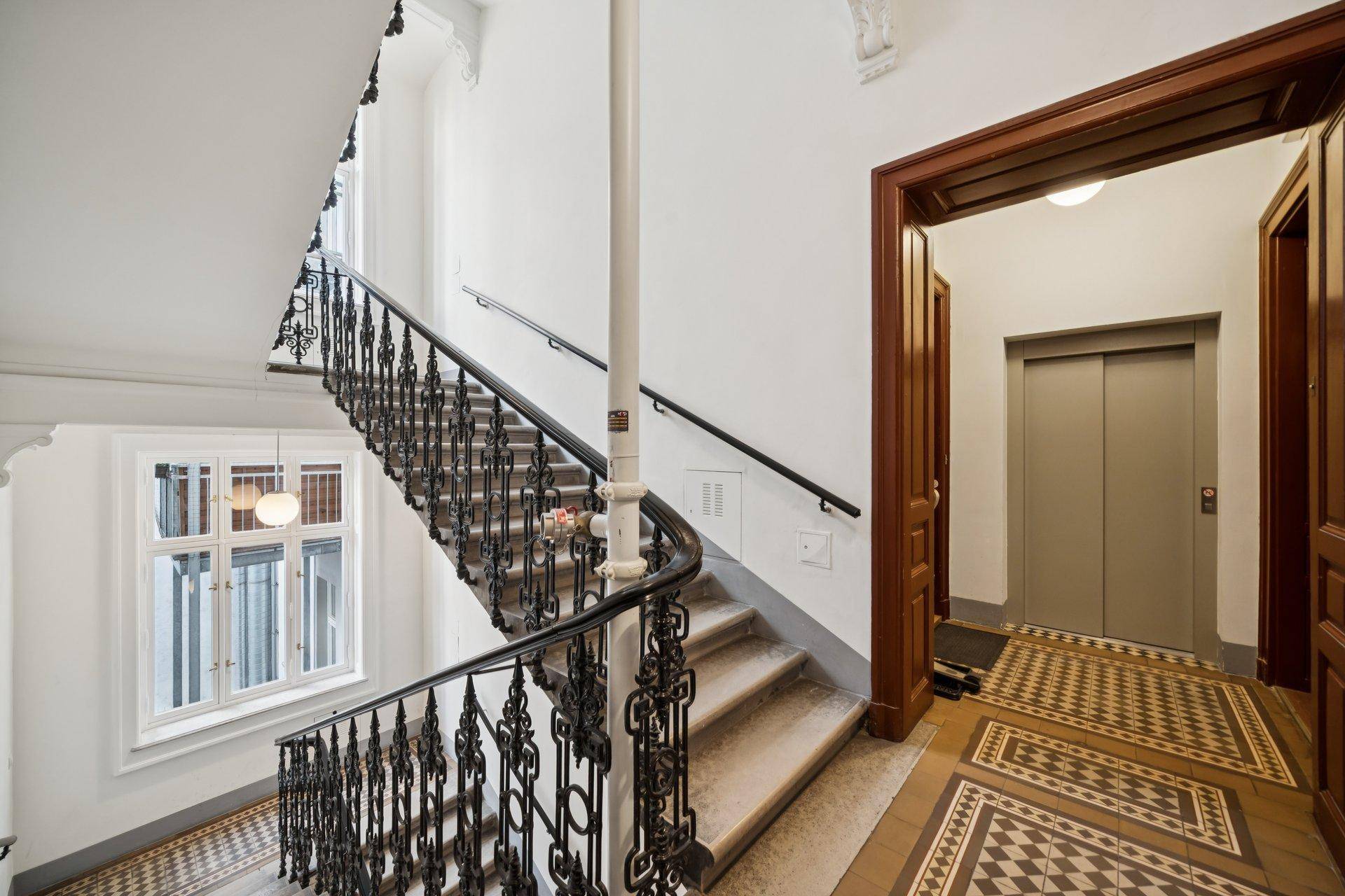 Historisches Treppenhaus mit kunstvollen Geländern und Zugang zum modernen Aufzug.
