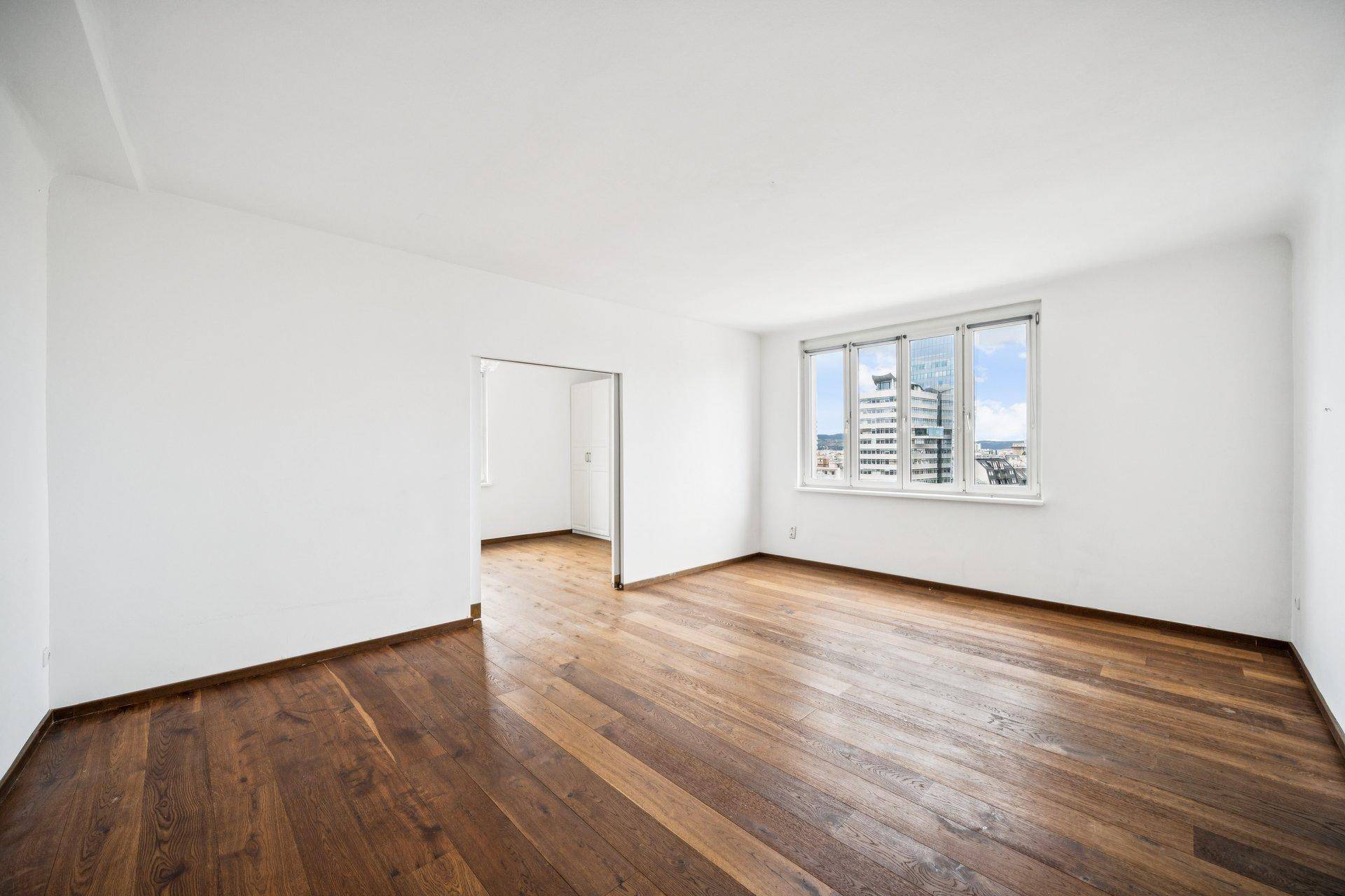 Geräumiger, heller Raum mit Holzboden und großem Fenster, bereit zur Einrichtung.