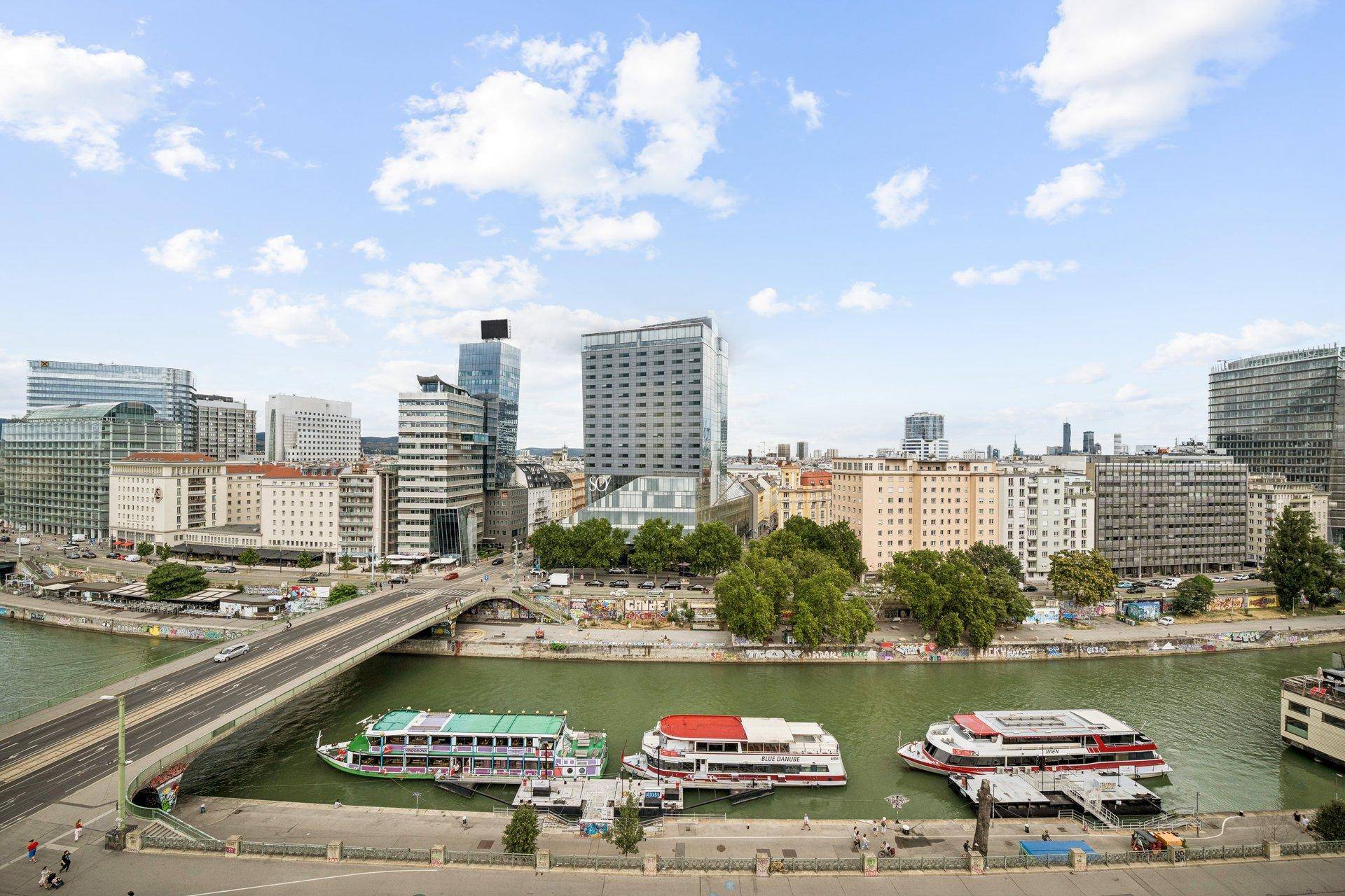 Weitläufiger Stadtblick mit Fluss, Brücken und modernen Gebäuden unter blauem Himmel.