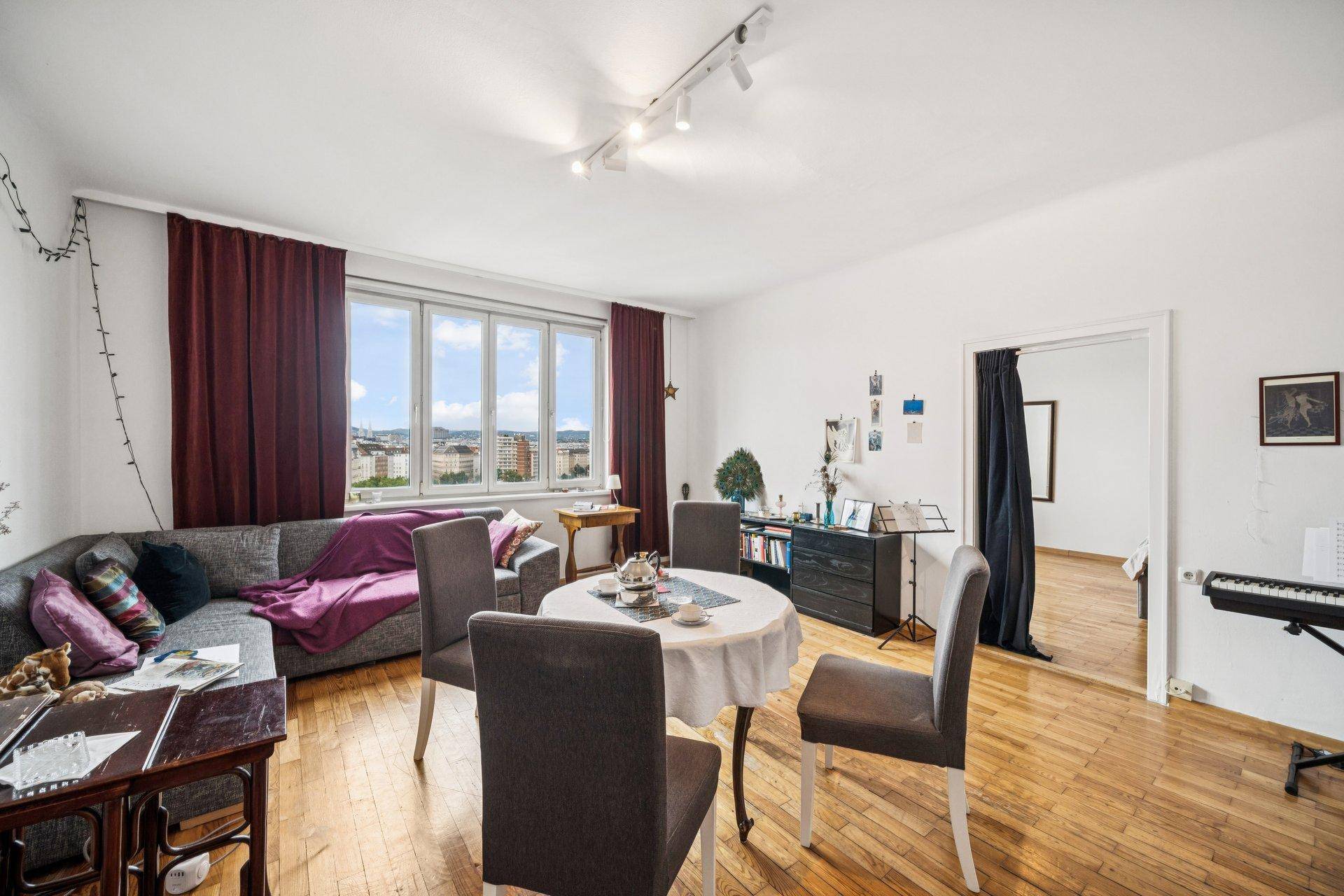 Gemütliches Wohnzimmer mit Holzboden, Esstisch und großem Fenster mit Stadtblick.