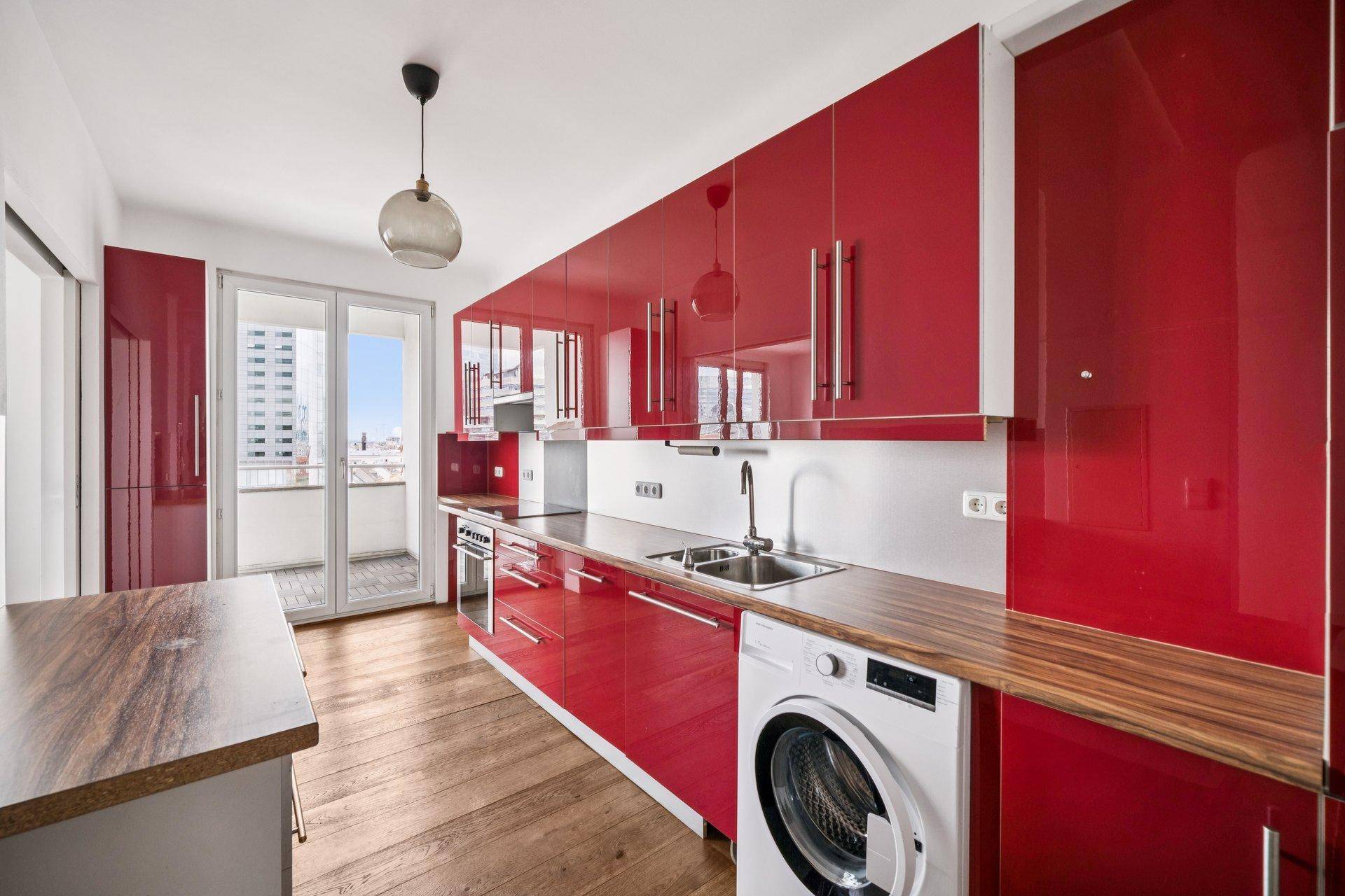 Moderne Küche mit glänzenden roten Fronten, Holzarbeitsplatte und Zugang zum Balkon.