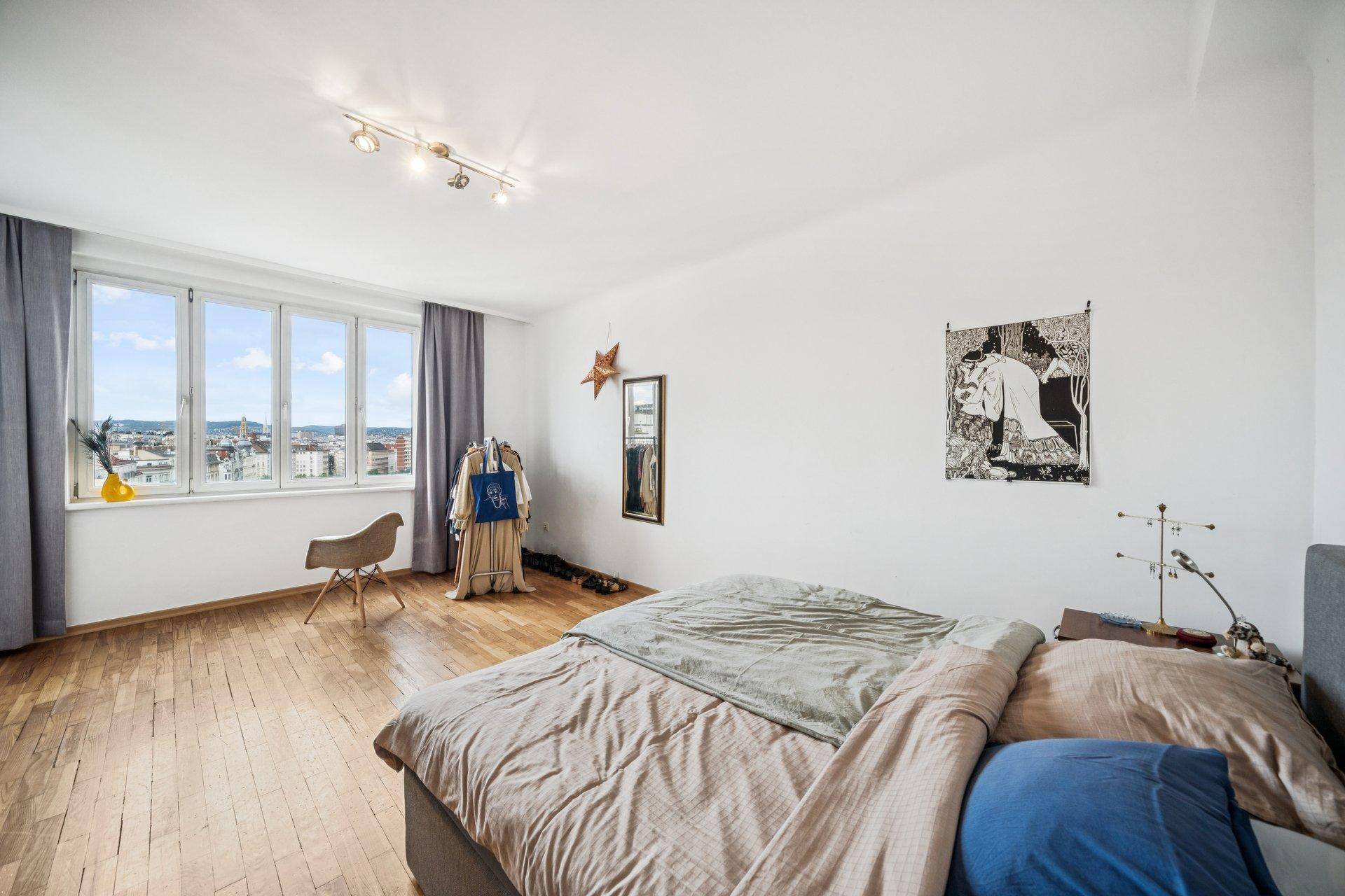 Helles Schlafzimmer mit Holzboden, großem Fenster und Blick auf die Stadt.