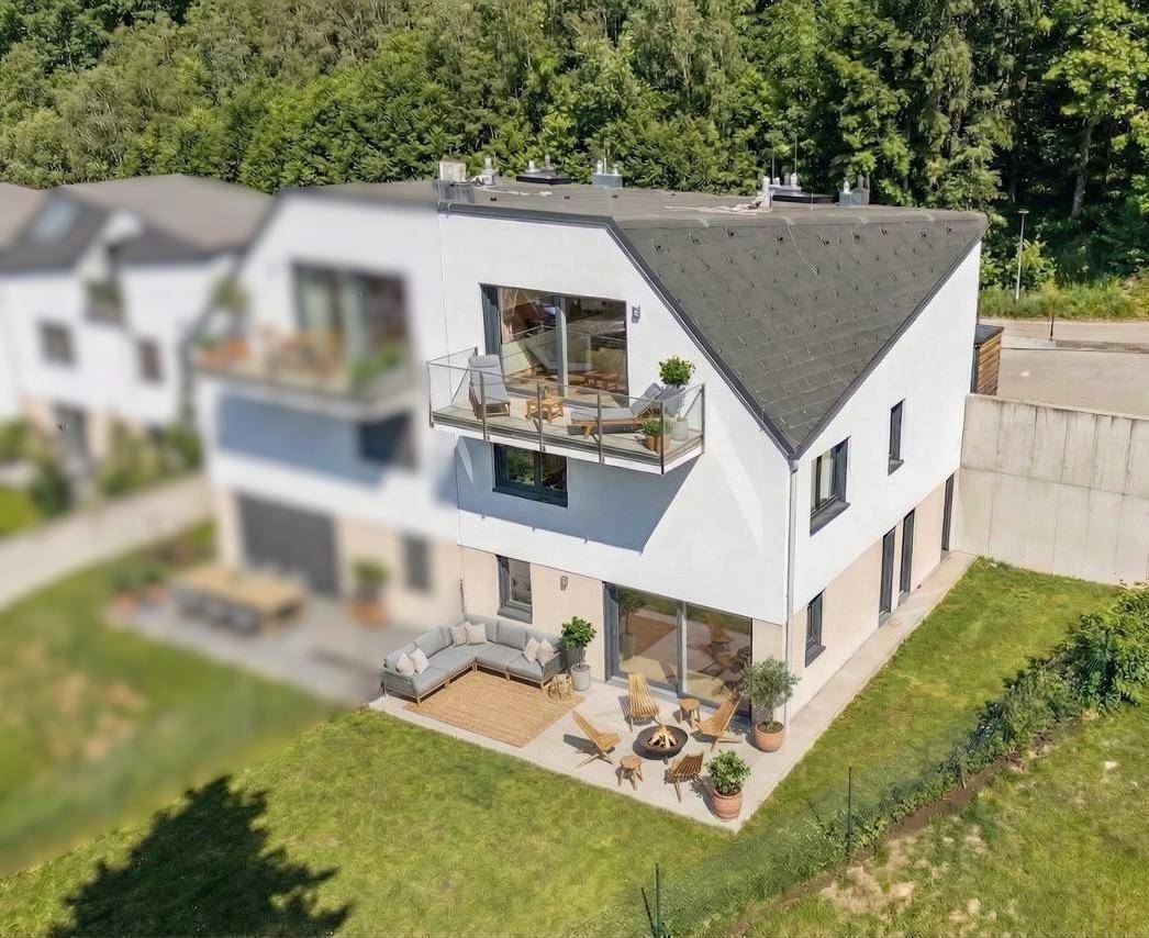 Luftaufnahme eines modernen Hauses mit Garten, Terrasse und Balkonen in grüner Umgebung.