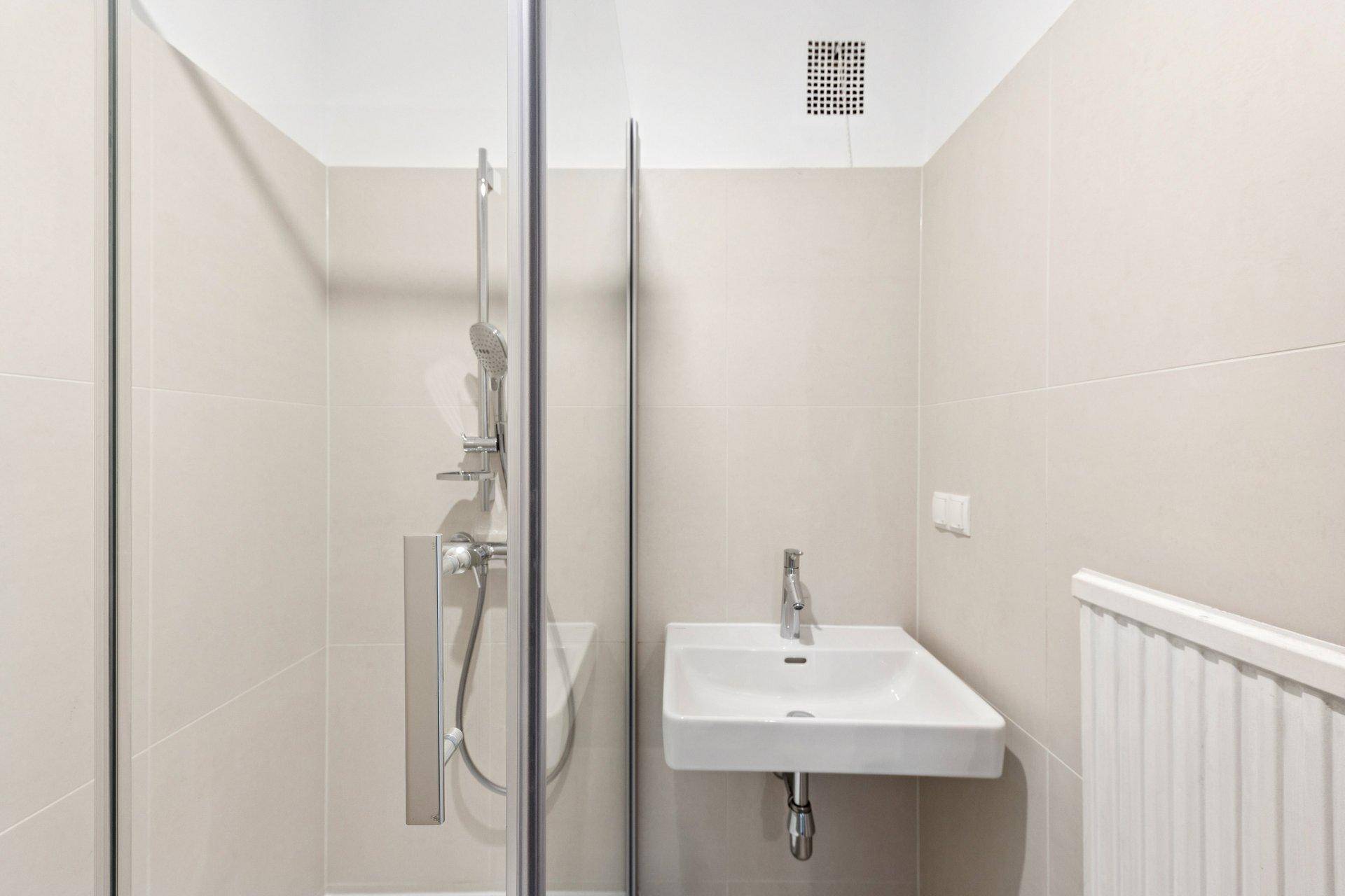Modernes Badezimmer mit Duschkabine, Waschbecken und hellen Fliesen.