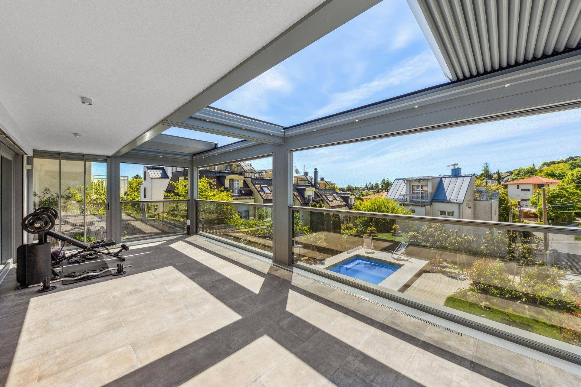 Geräumige überdachte Terrasse mit Fitnessgeräten und Blick auf einen Whirlpool im Garten.