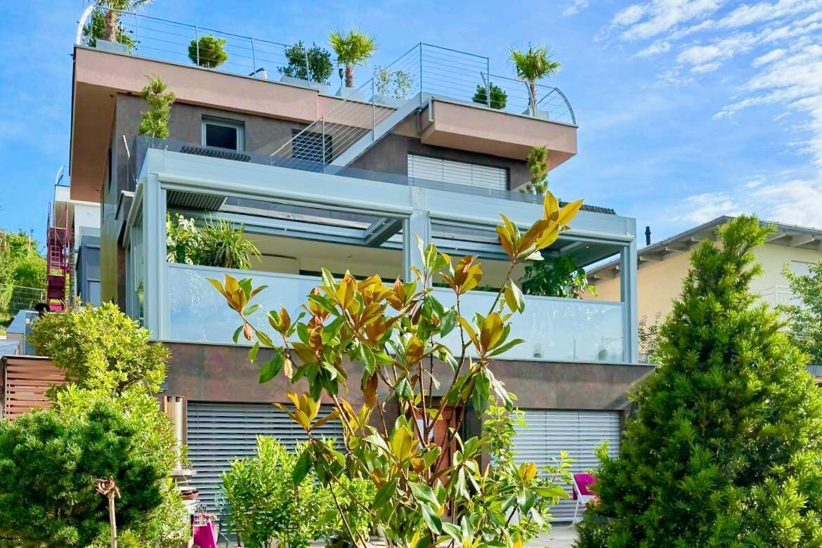 Ansicht der modernen Hausfassade mit großen Glasflächen und üppiger Bepflanzung im Vordergrund.
