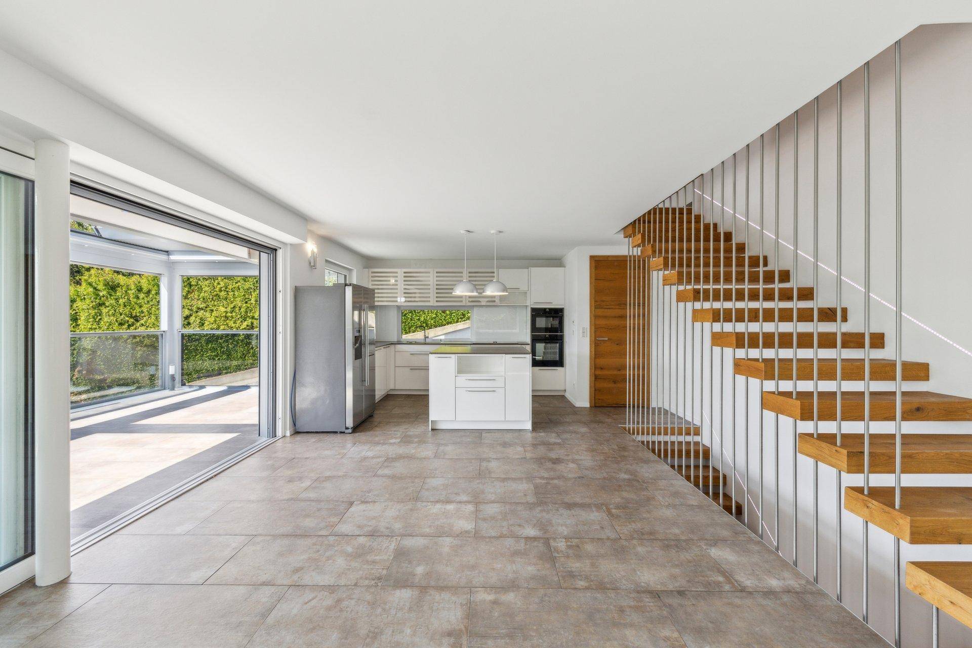 Heller offener Wohnbereich mit moderner Küche, Fliesenboden und eleganter Holztreppe.