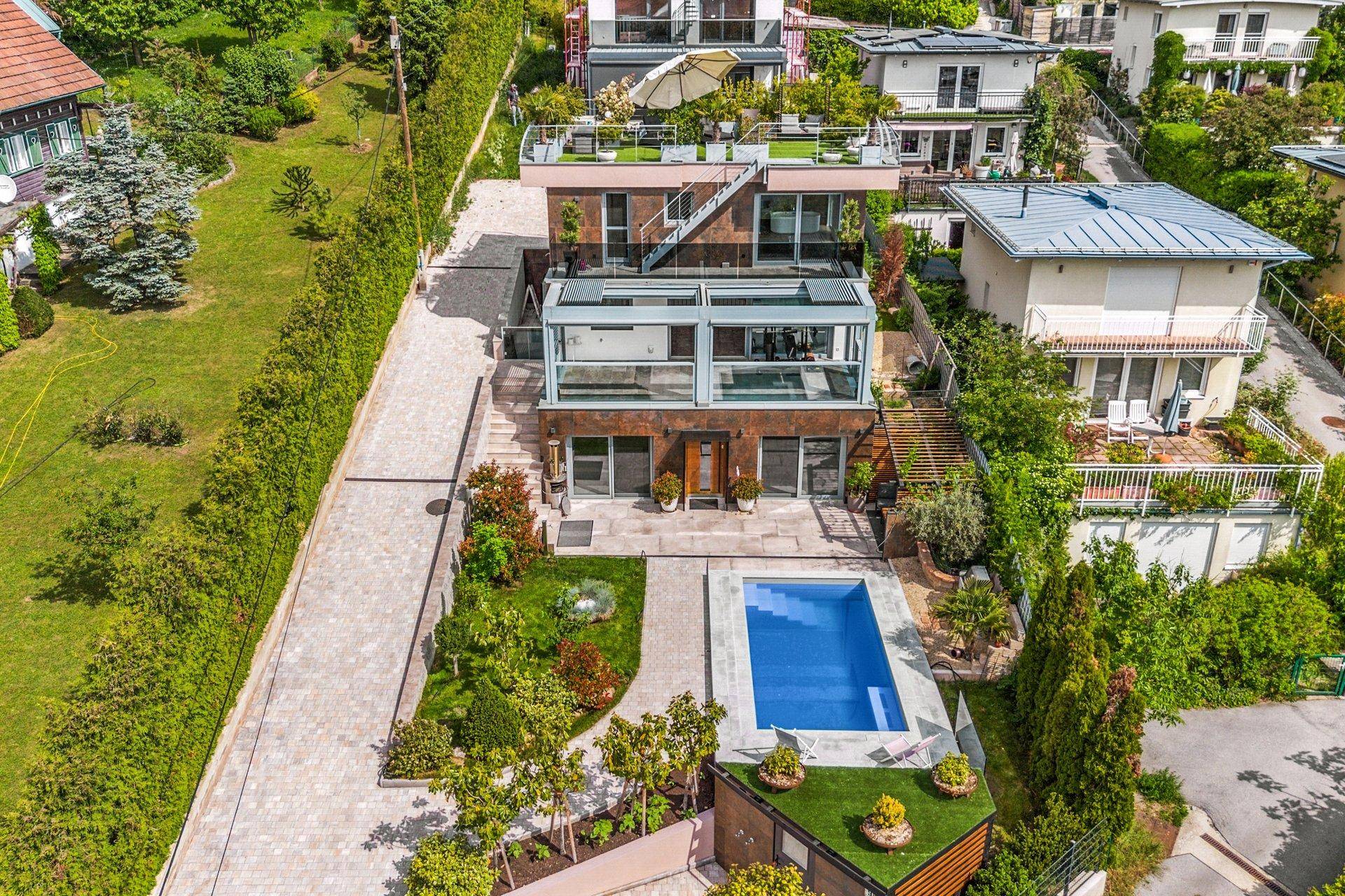 Luftaufnahme der modernen Villa mit Pool, weitläufigem Garten und umliegender Wohnbebauung.