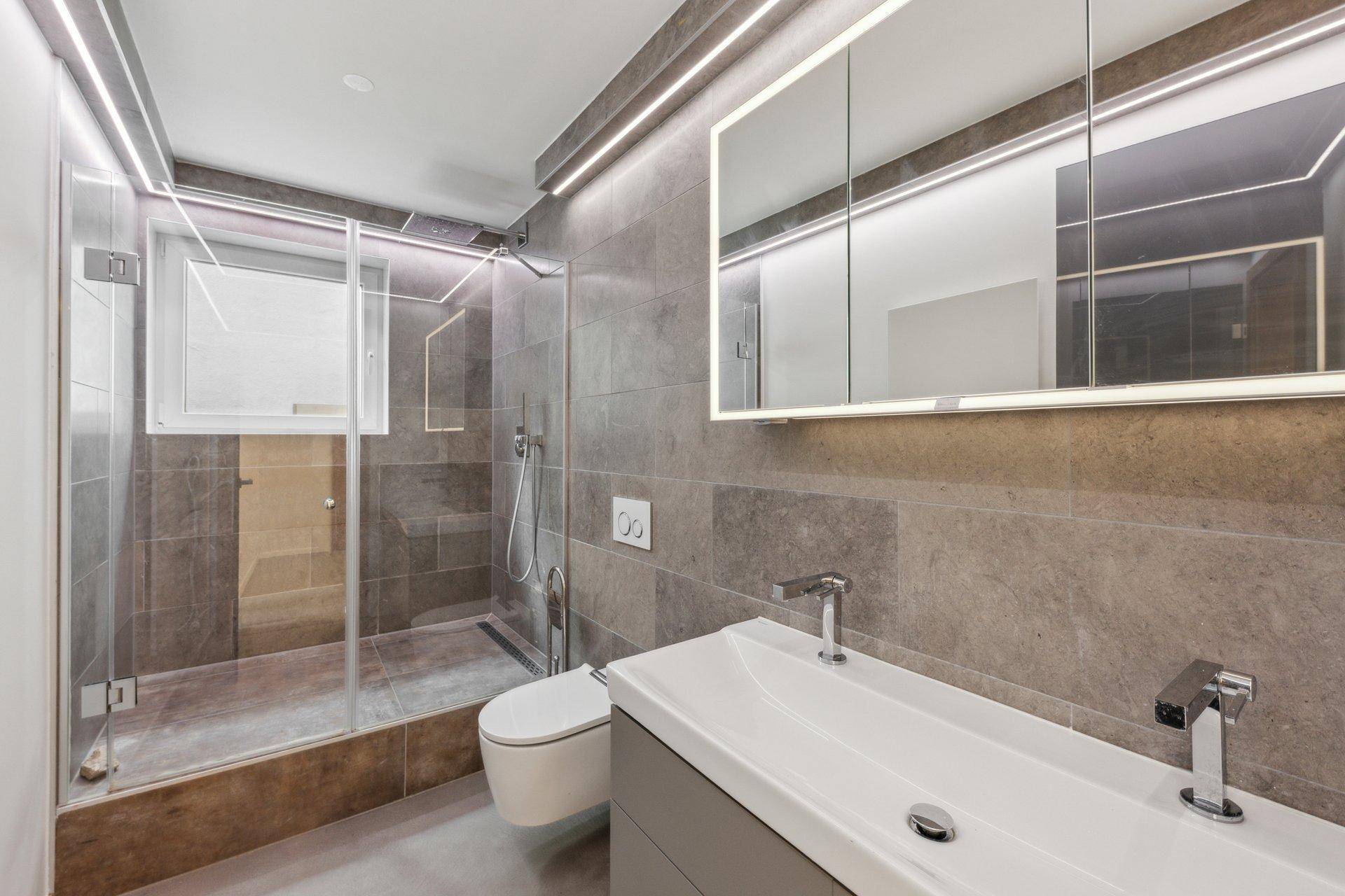 Modernes Badezimmer mit begehbarer Dusche, Wand-WC und beleuchtetem Spiegelschrank.