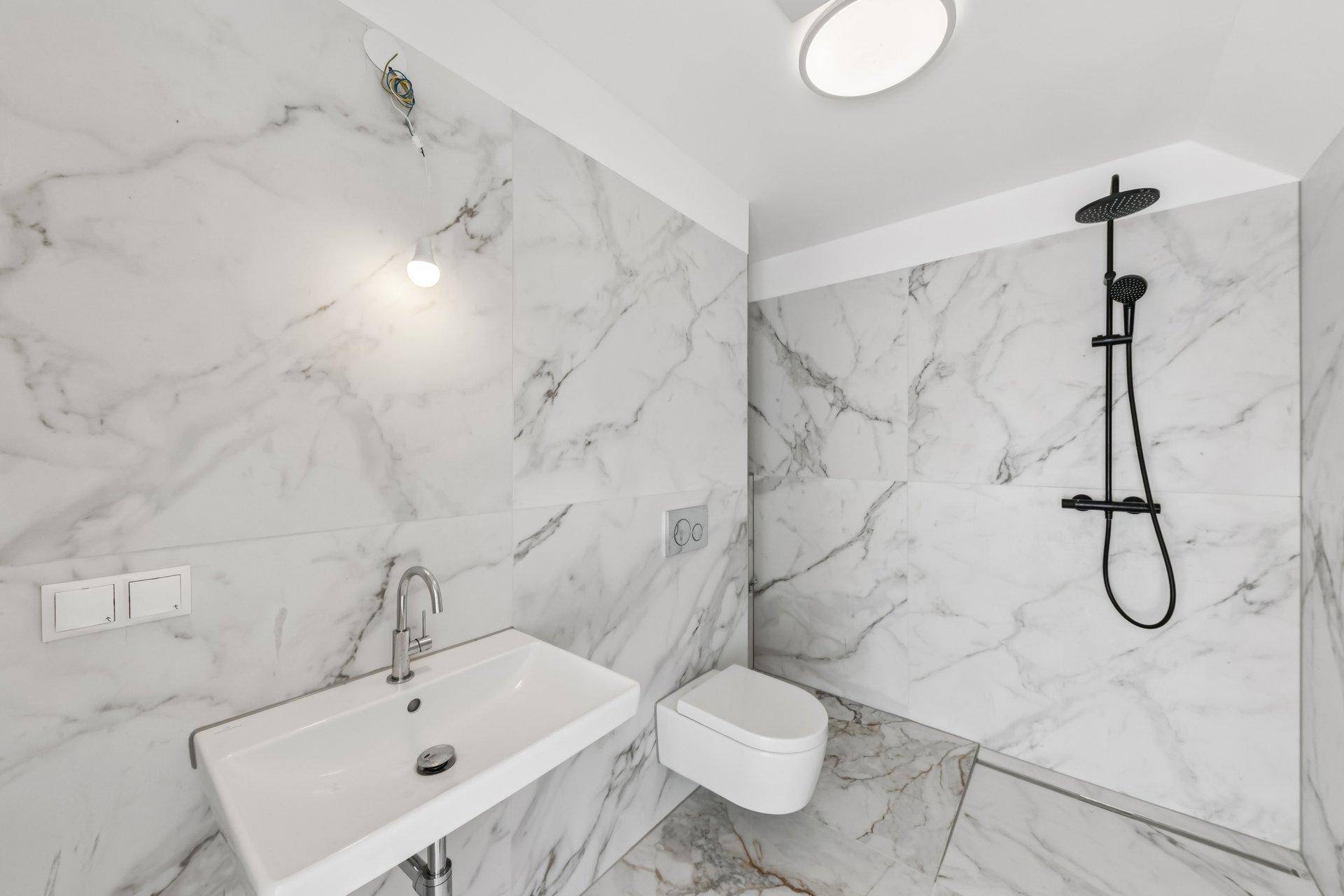 Modernes Badezimmer mit Marmorfliesen, bodengleicher Dusche und Wand-WC.