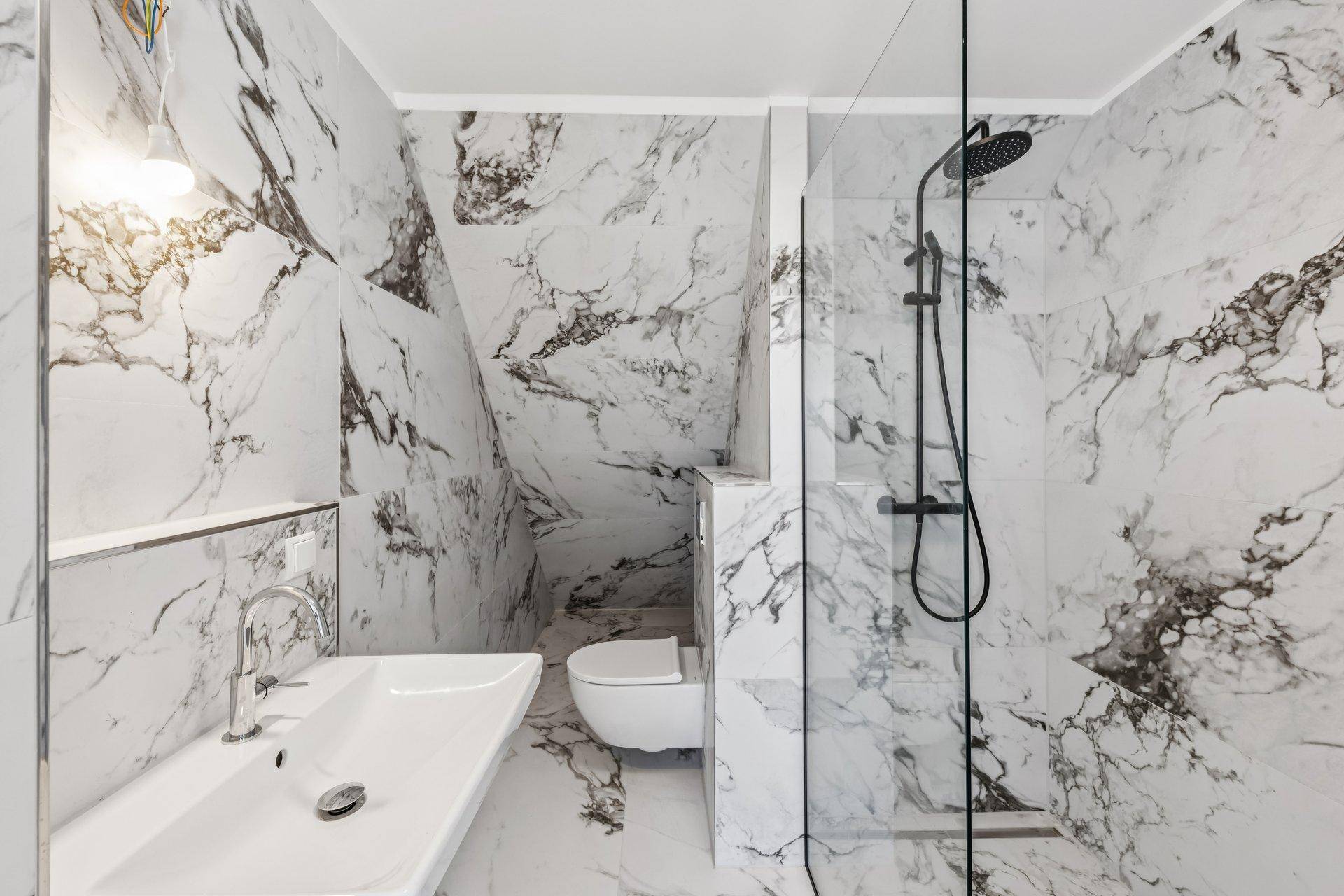 Modernes Badezimmer mit Marmorfliesen, bodengleicher Dusche und wandhängendem WC.