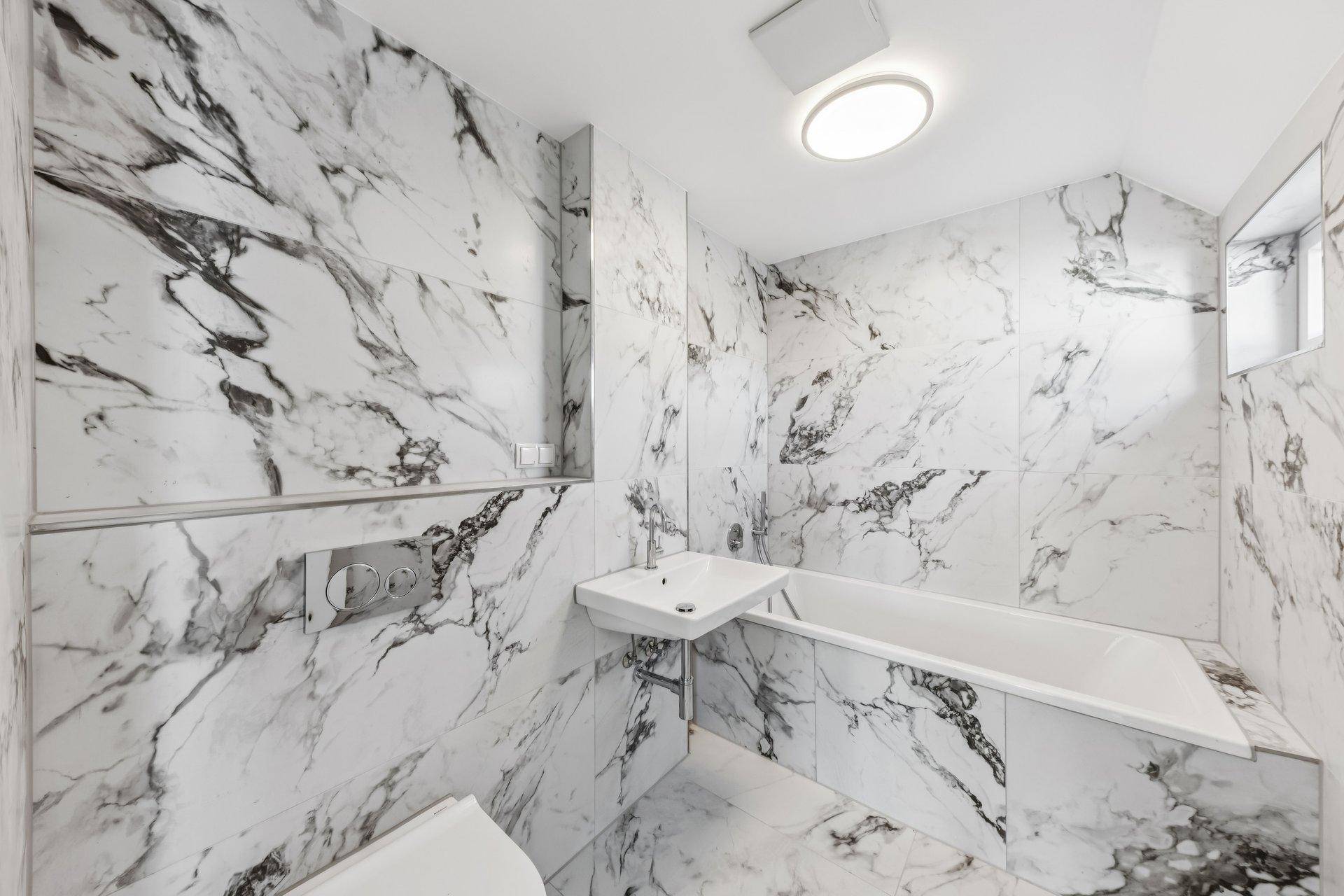 Elegantes Badezimmer mit großformatigen Marmorfliesen, Badewanne und modernem Waschtisch.
