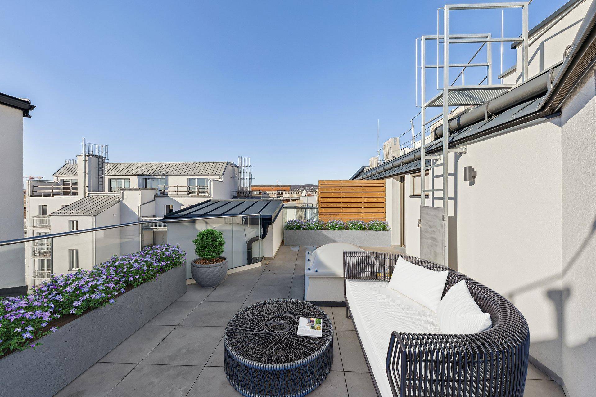 Geräumige Dachterrasse mit modernen Loungemöbeln, Pflanzen und weitem Blick über die Stadt.