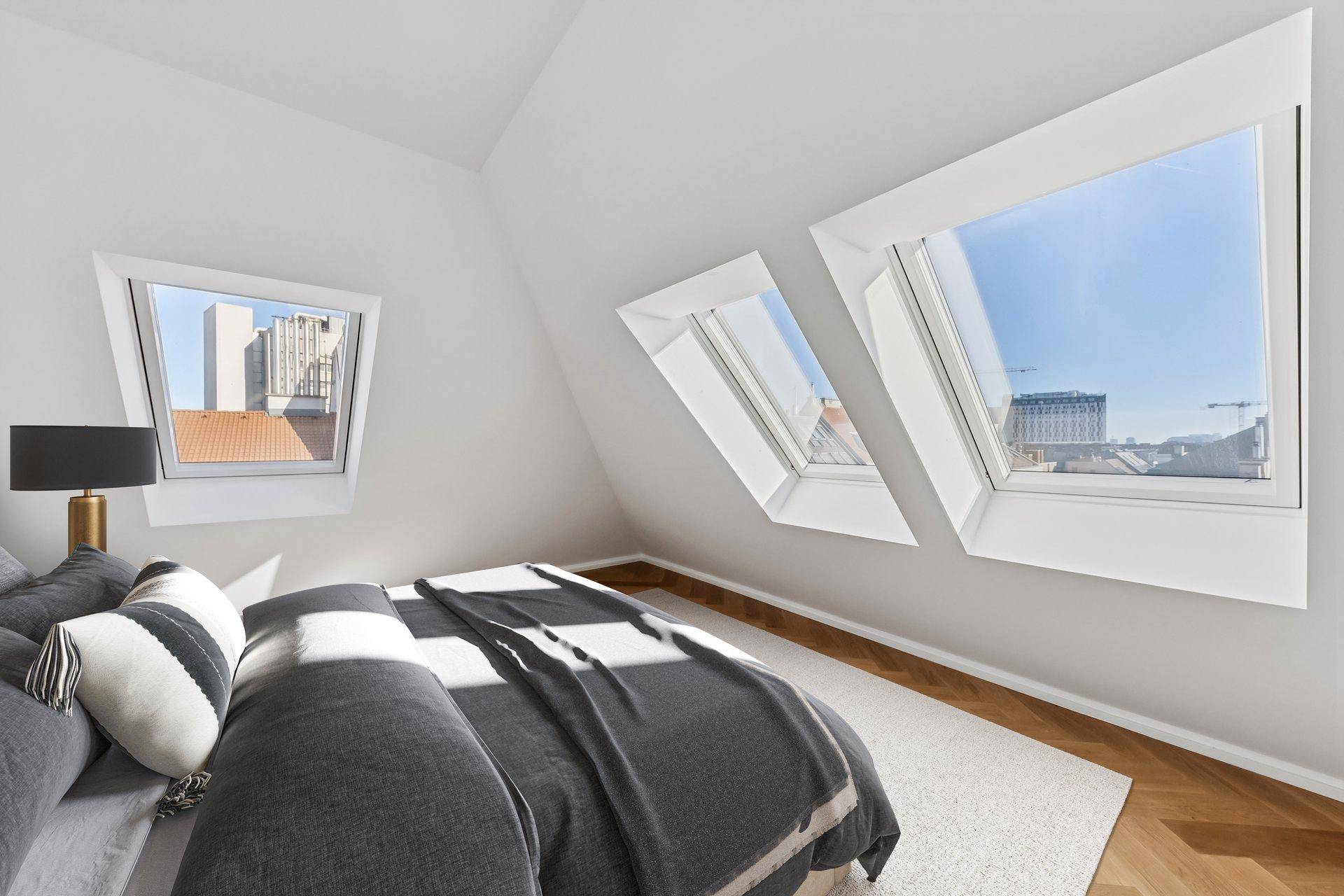 Helles Schlafzimmer im Dachgeschoss mit schrägen Wänden, Dachfenstern und Stadtblick.