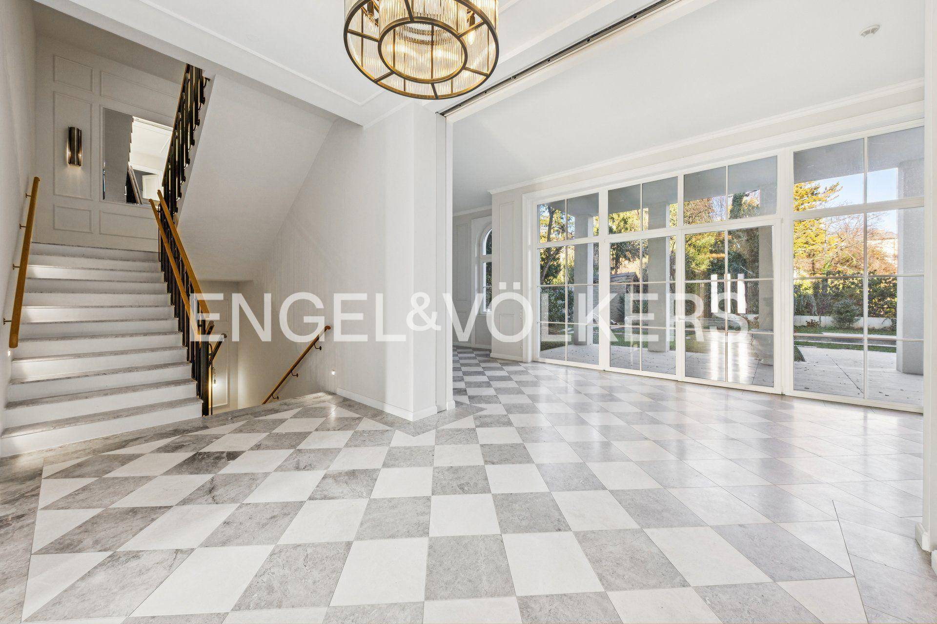 Elegante Eingangshalle mit Marmorboden, breiter Treppe und großen Fenstern zum Garten.