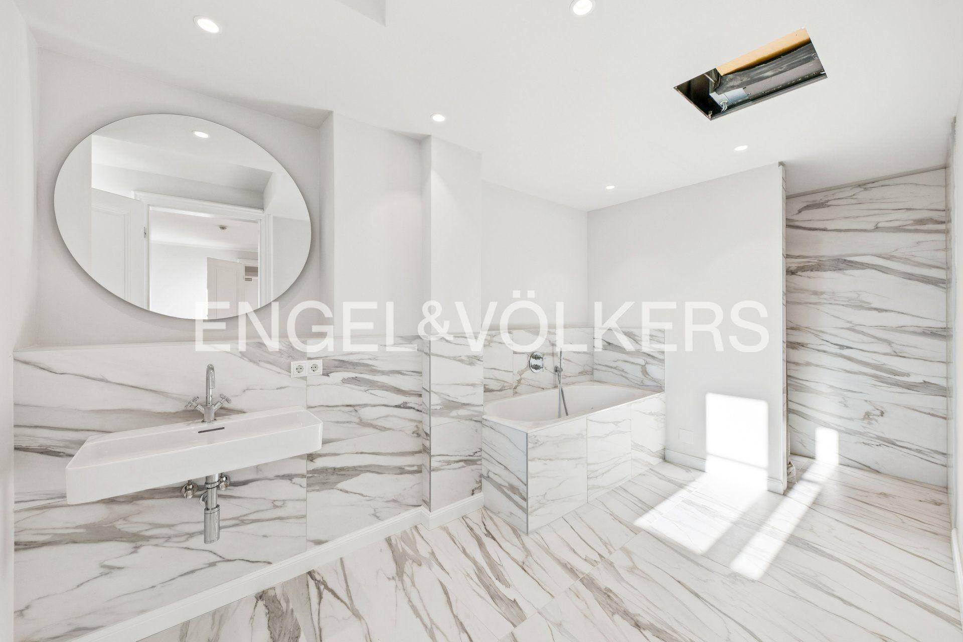 Elegantes Badezimmer mit Marmorfliesen, integrierter Badewanne und modernem Waschbecken.