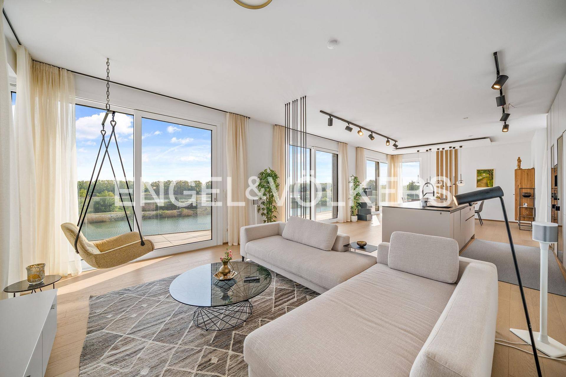 Gemütliches Wohnzimmer mit modernen Sofas, Schaukelstuhl und weitem Blick auf den See.