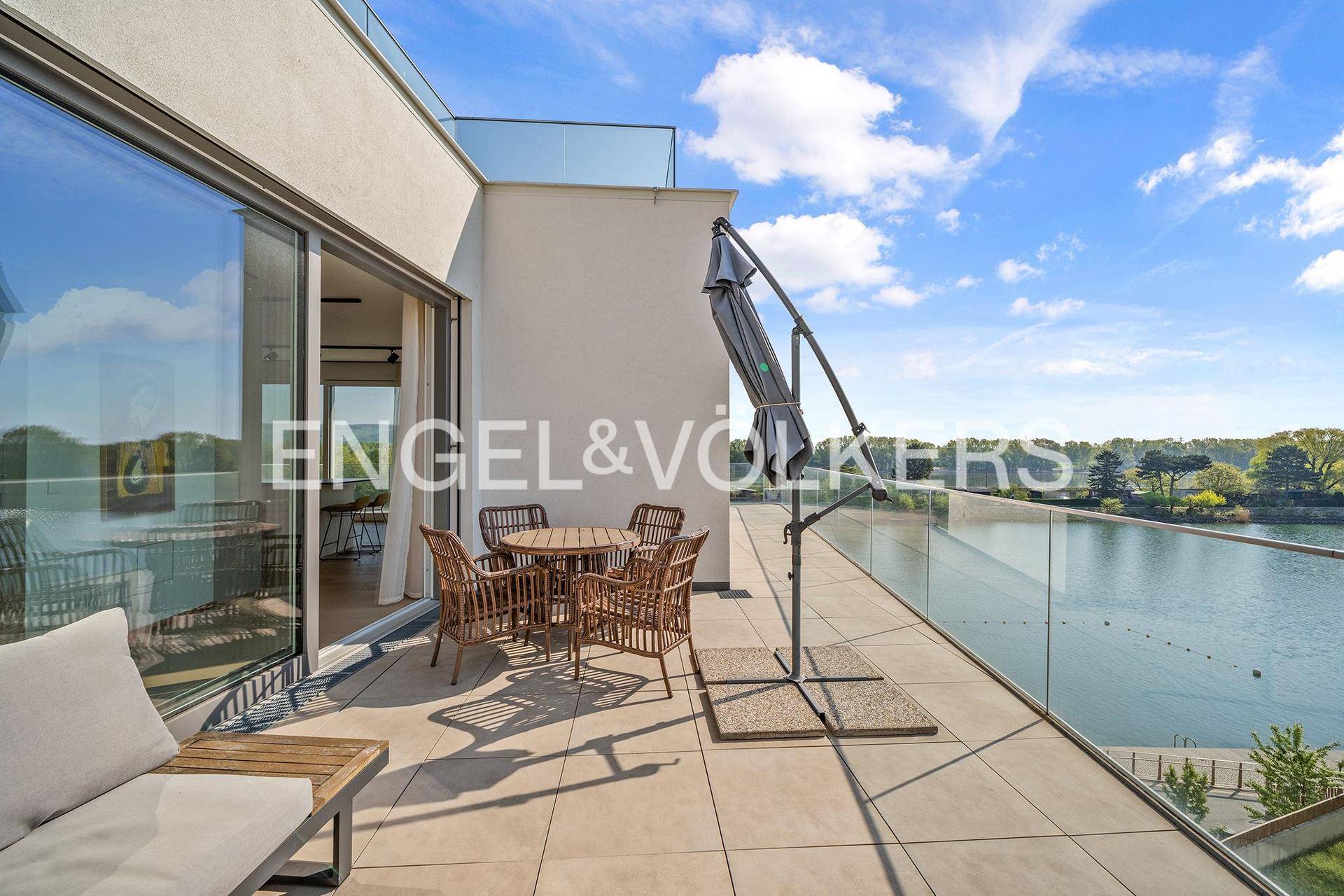 Große Terrasse mit modernen Outdoor-Möbeln, Sonnenschirm und Panoramablick auf den See.
