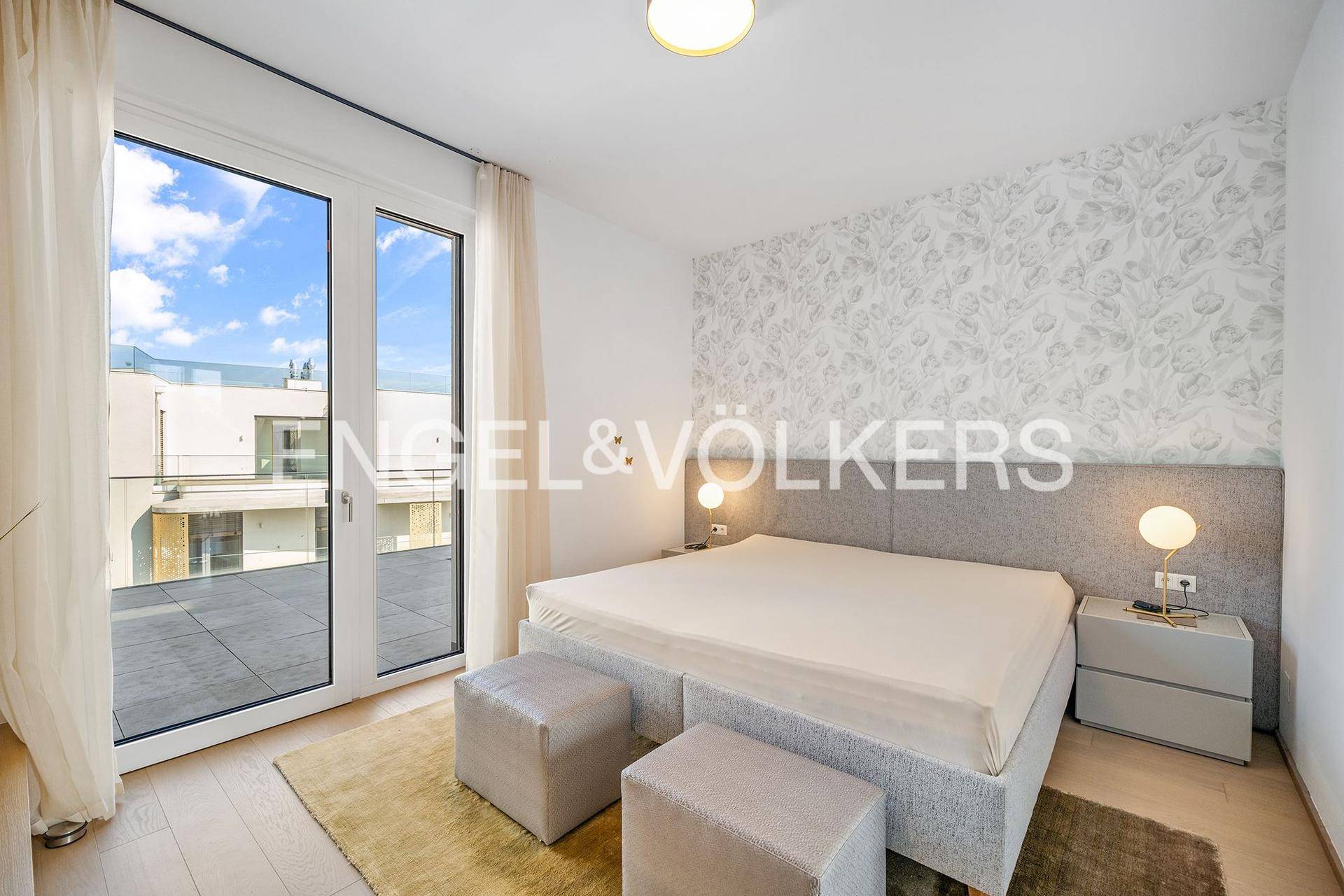 Helles Schlafzimmer mit großem Bett, gemusterter Tapete und Zugang zu einer Außenterrasse.