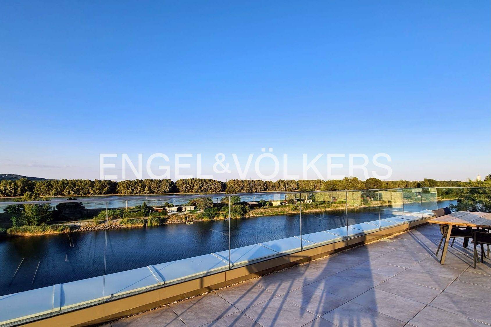 Große Dachterrasse mit Glasgeländer, Esstisch und weitem Blick über den See.