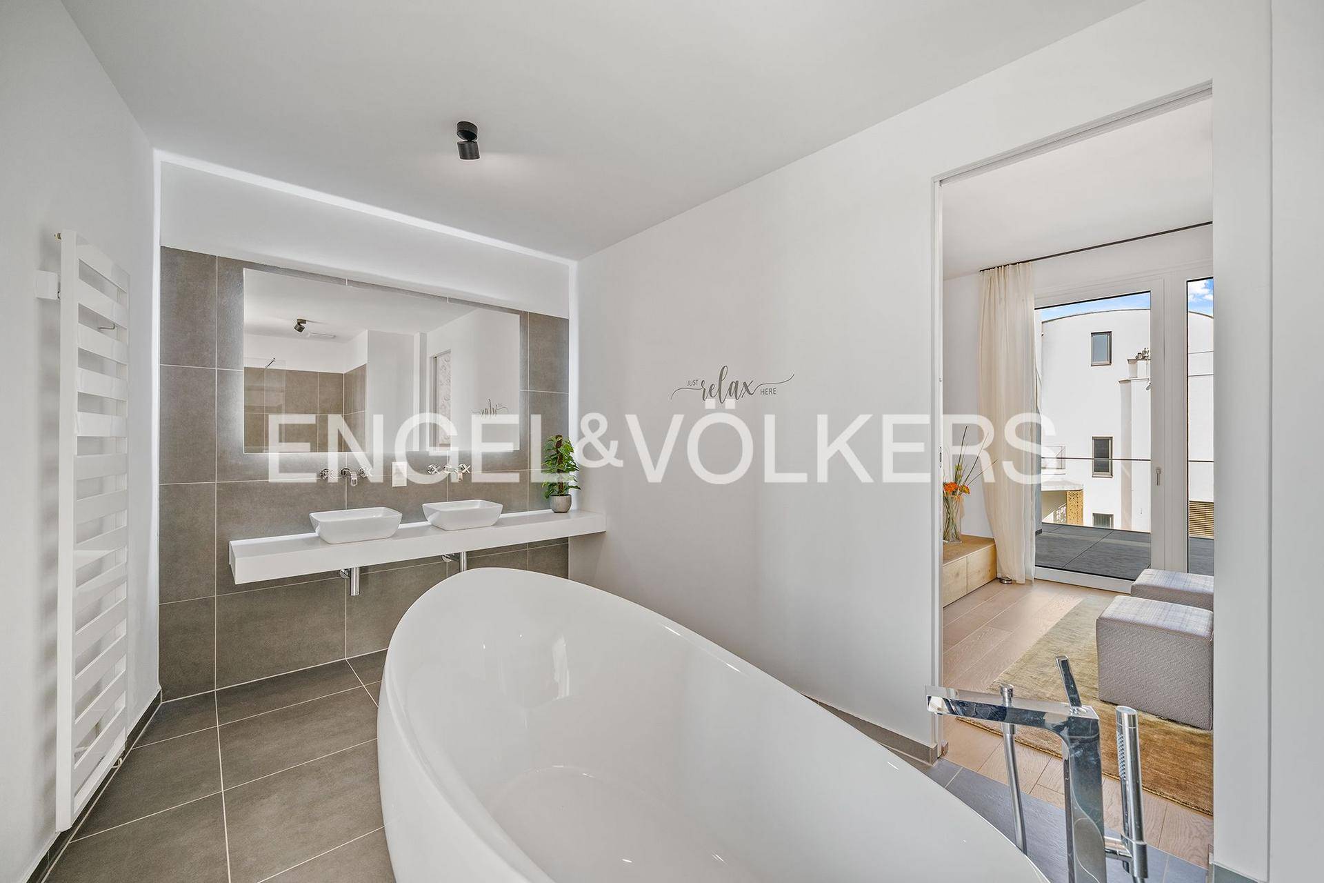 Modernes Badezimmer mit freistehender Badewanne, Doppelwaschbecken und Zugang zu einem weiteren Raum.