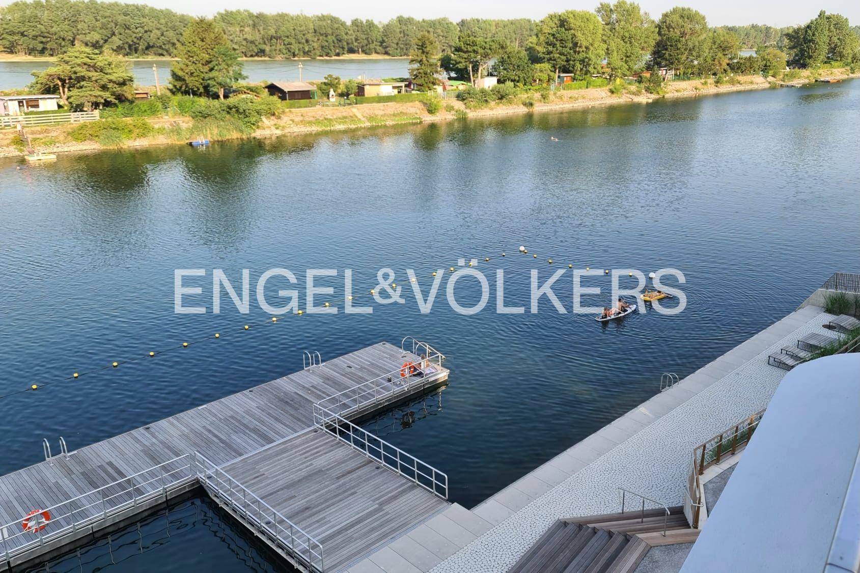 Blick auf den See mit Bootsstegen und Bademöglichkeiten, umgeben von grüner Natur.