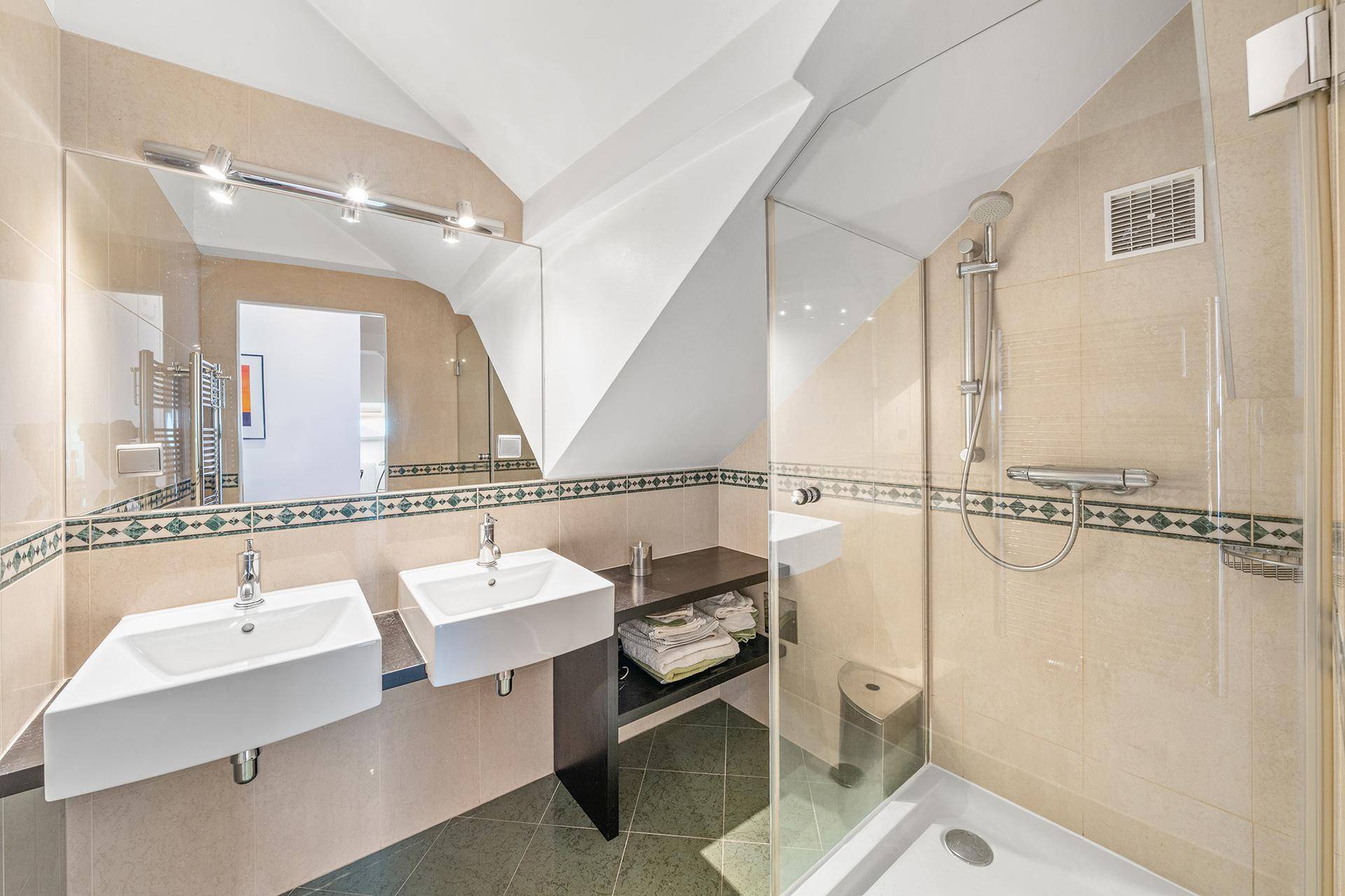 Modernes Badezimmer mit Doppelwaschbecken, Duschkabine und dekorativen Fliesen.