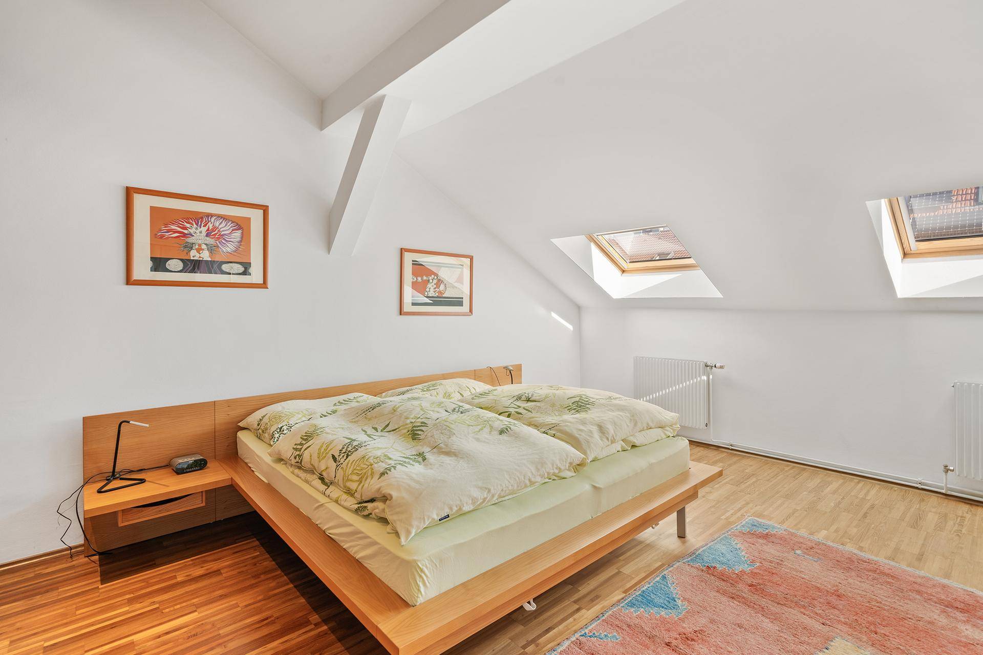 Schlafzimmer mit Holzboden, Dachschrägen und zwei Dachfenstern für viel Tageslicht.