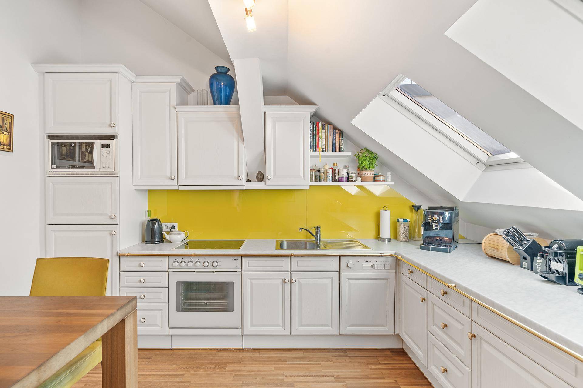 Helle Küche mit weißen Schränken, gelber Rückwand und Dachfenster für natürliches Licht.