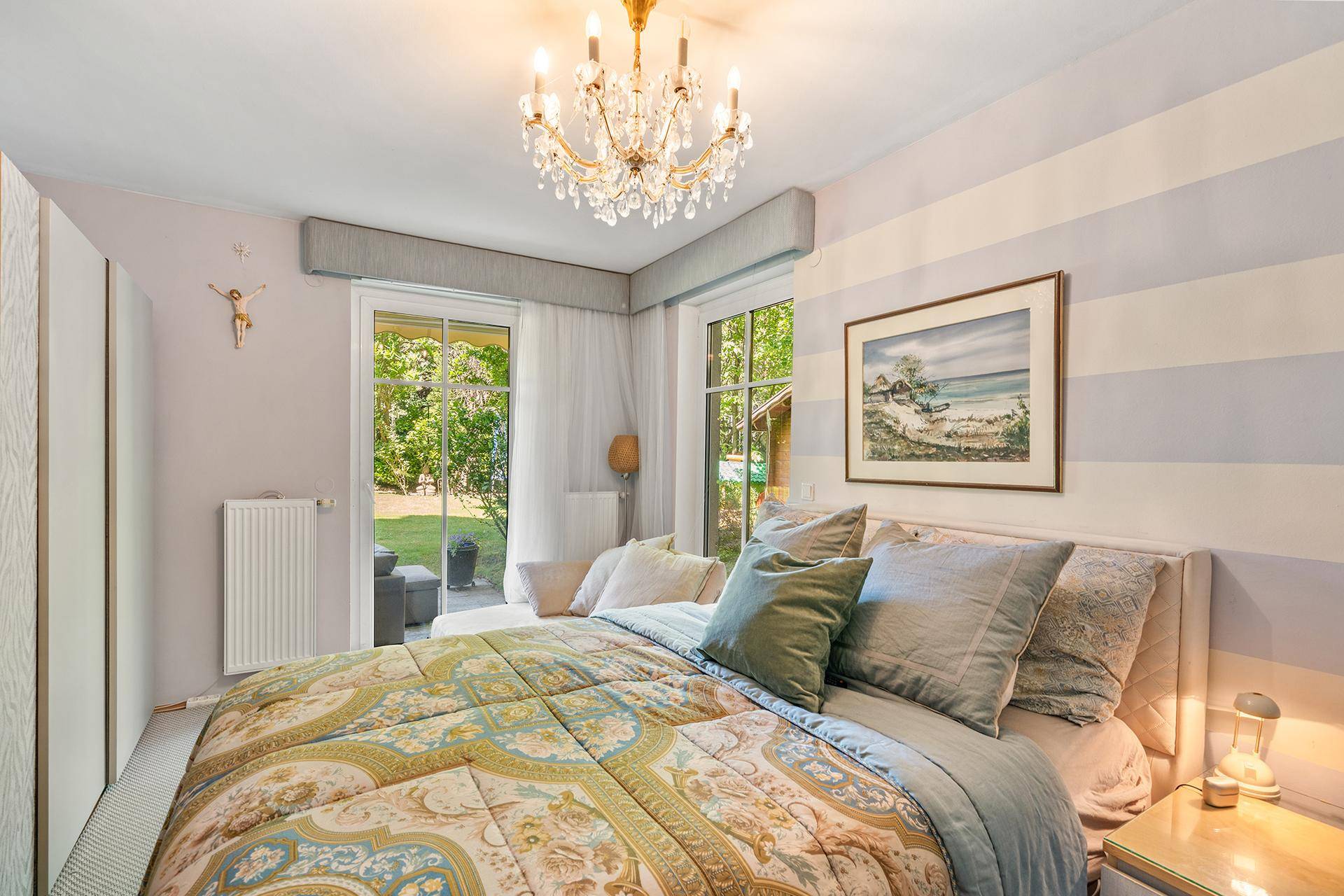 Helles Schlafzimmer mit großem Bett, elegantem Kronleuchter und direktem Zugang zu einem Außenbereich.
