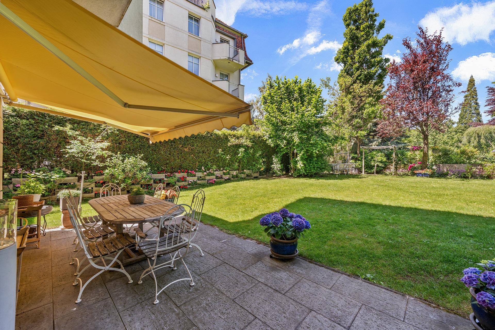 Sonniger Terrassenbereich mit Esstisch, Markise und weitem Blick über den gepflegten Garten.