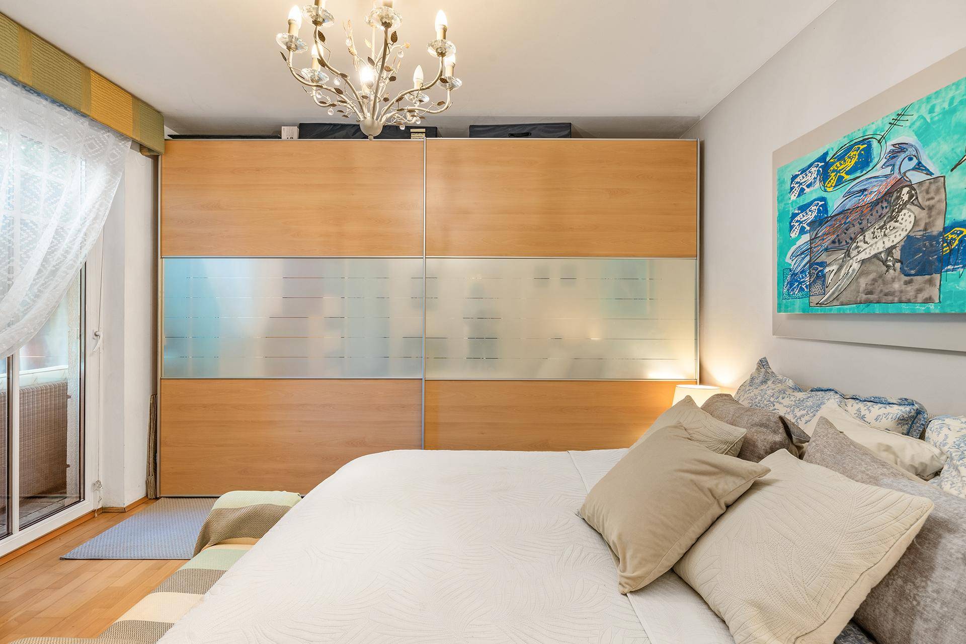Schlafzimmer mit großem Einbauschrank, modernem Kunstwerk und Zugang zu einem kleinen Balkon.