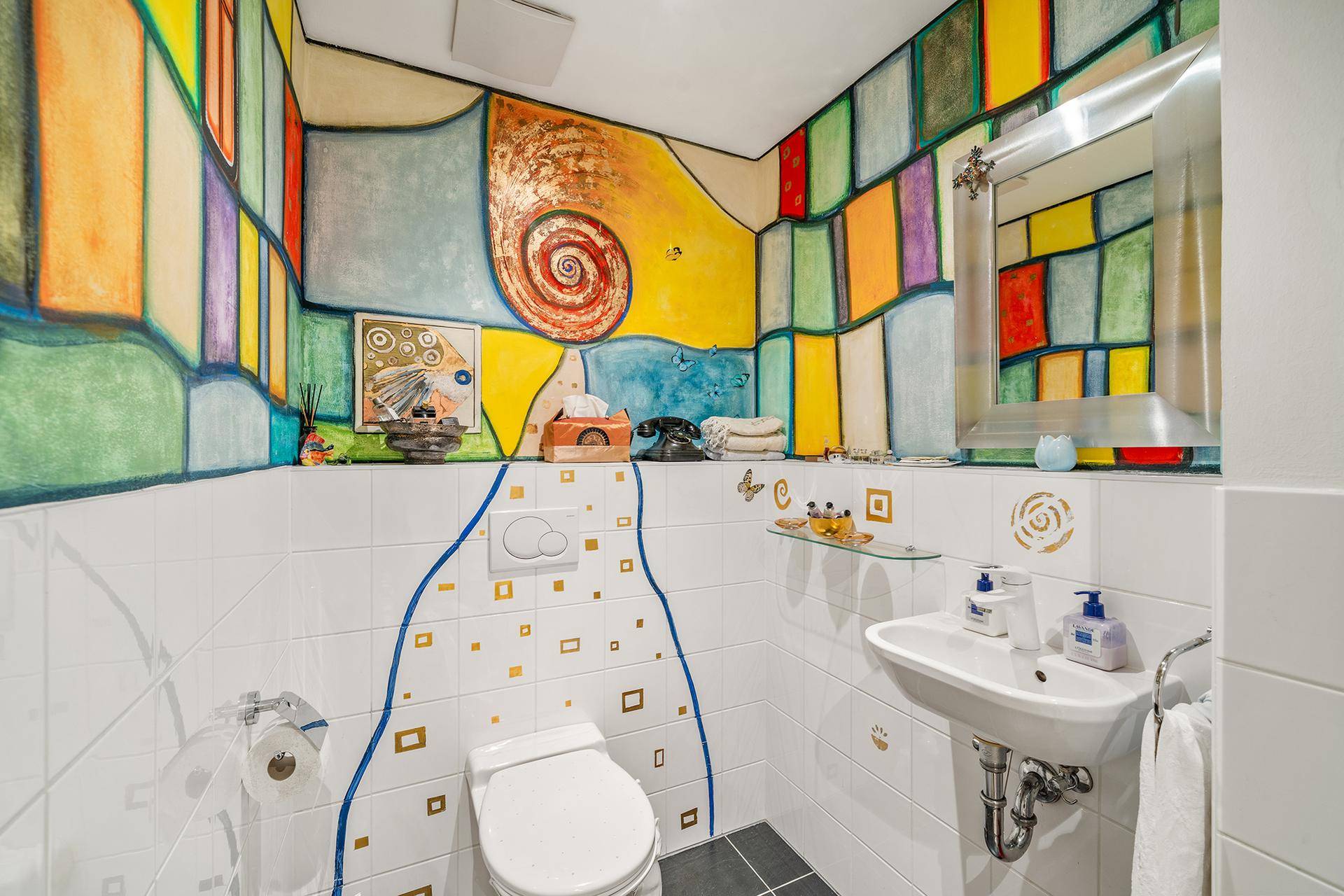 Farbenfrohes Gäste-WC mit künstlerischer Wandgestaltung, kleinem Waschbecken und Wand-WC.