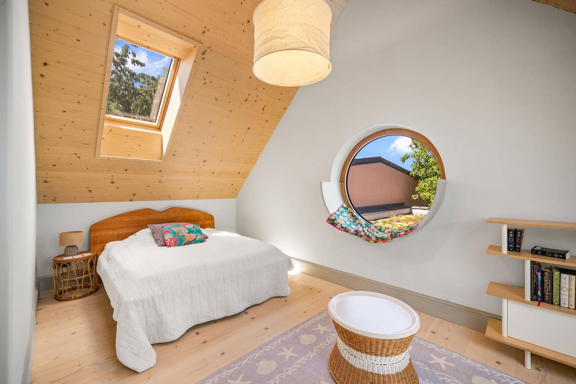 Helles Dachschlafzimmer mit Holzdecke, Dachfenster und einem einzigartigen runden Fenster.