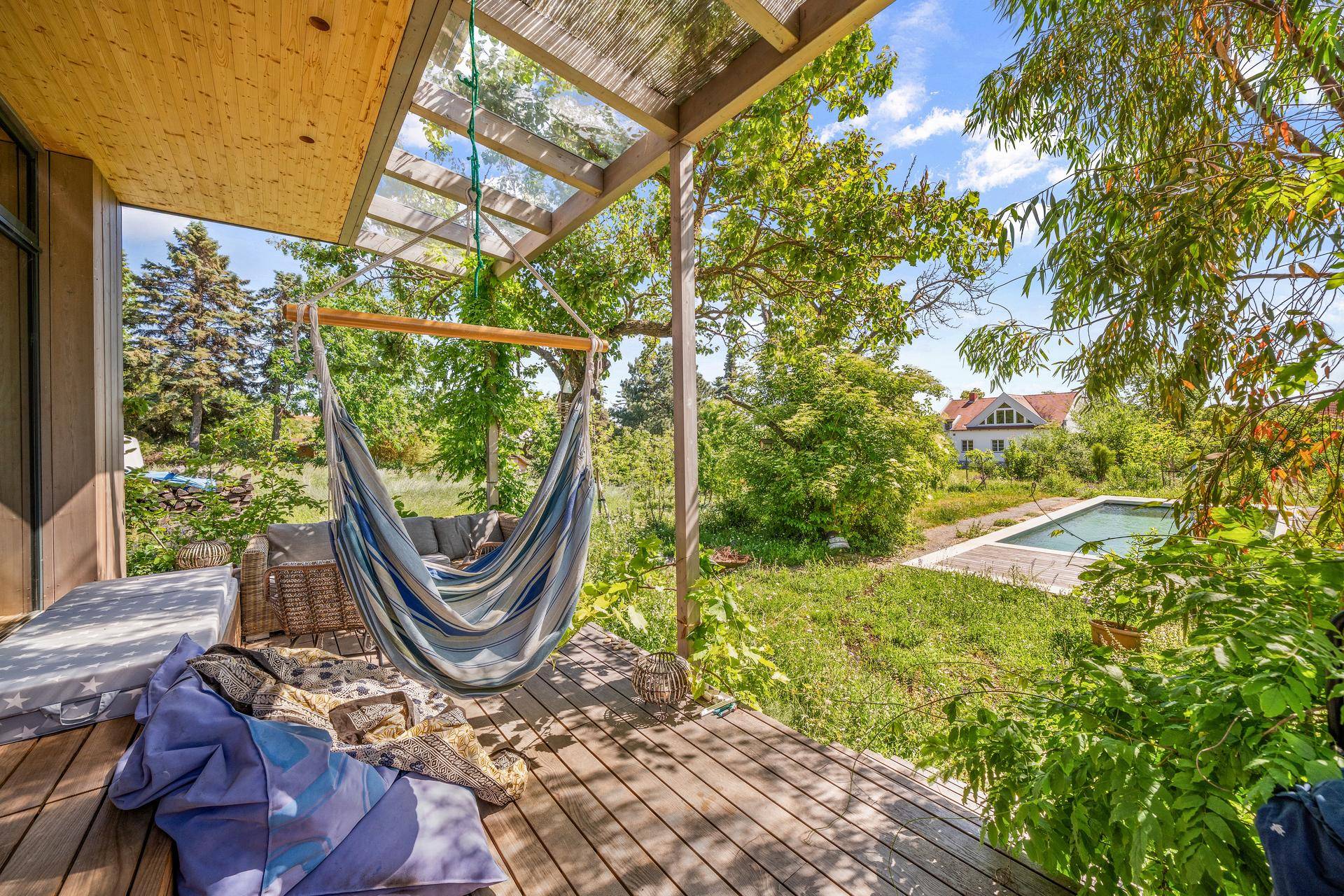 Gemütliche Holzterrasse mit Hängematte, Sitzgelegenheiten und Blick auf den Garten mit Pool.