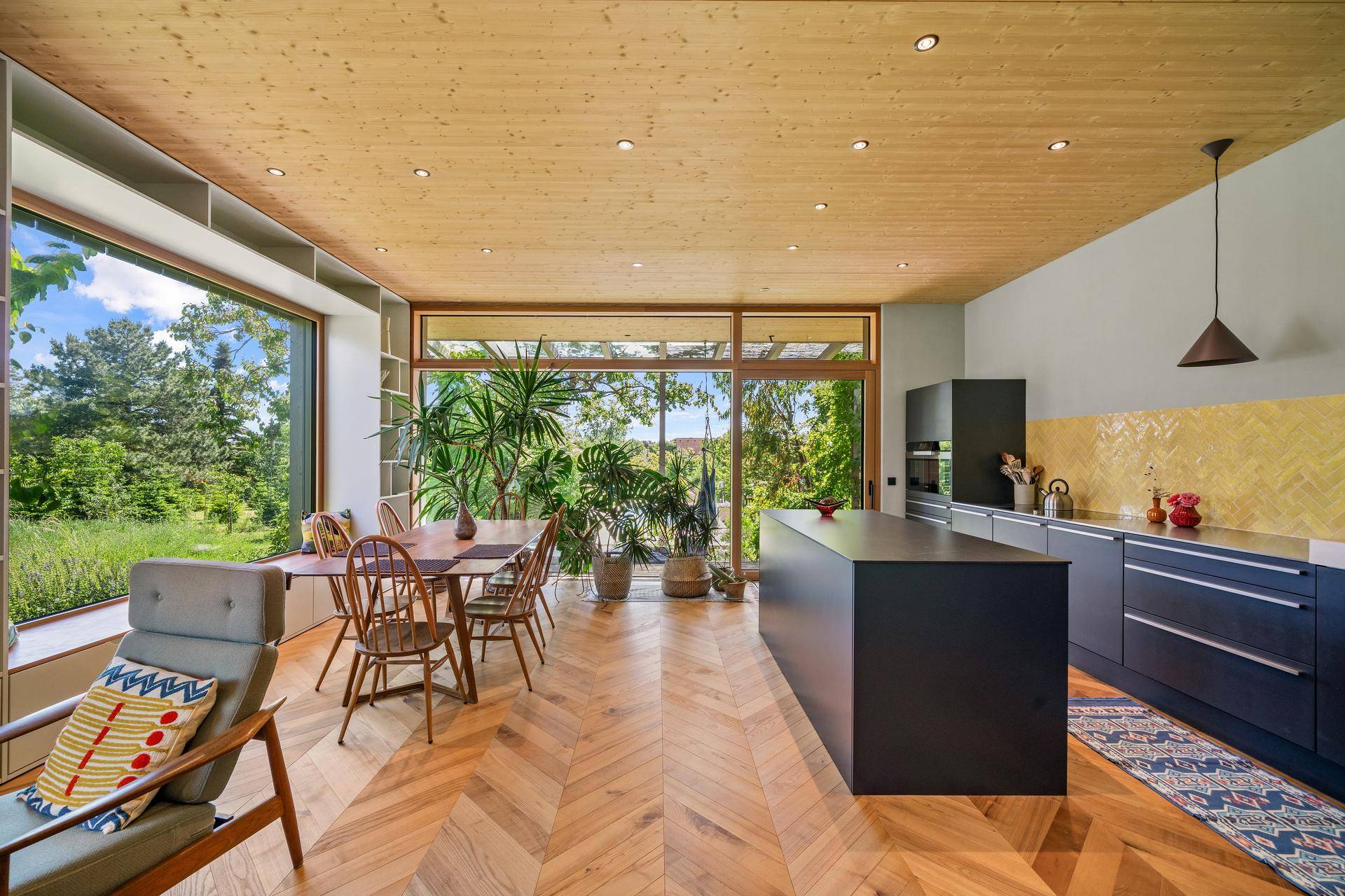 Moderner offener Wohn-Essbereich mit Kücheninsel, Holzboden und großen Fenstern zum Garten.