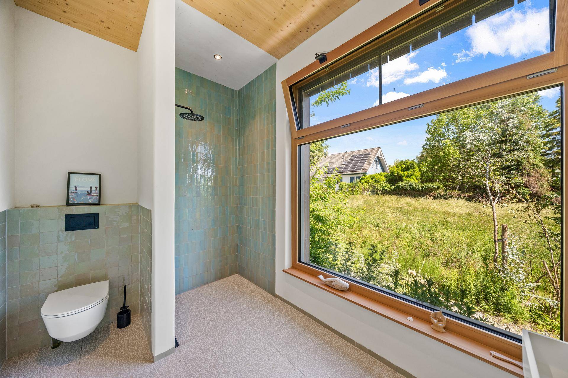 Modernes Badezimmer mit begehbarer Dusche, Wand-WC und großem Fenster mit Blick ins Grüne.