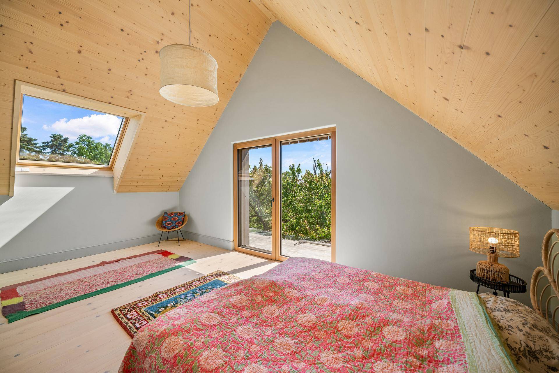 Dachschlafzimmer mit Holzdecke, Dachfenster und Zugang zu einem kleinen Balkon.