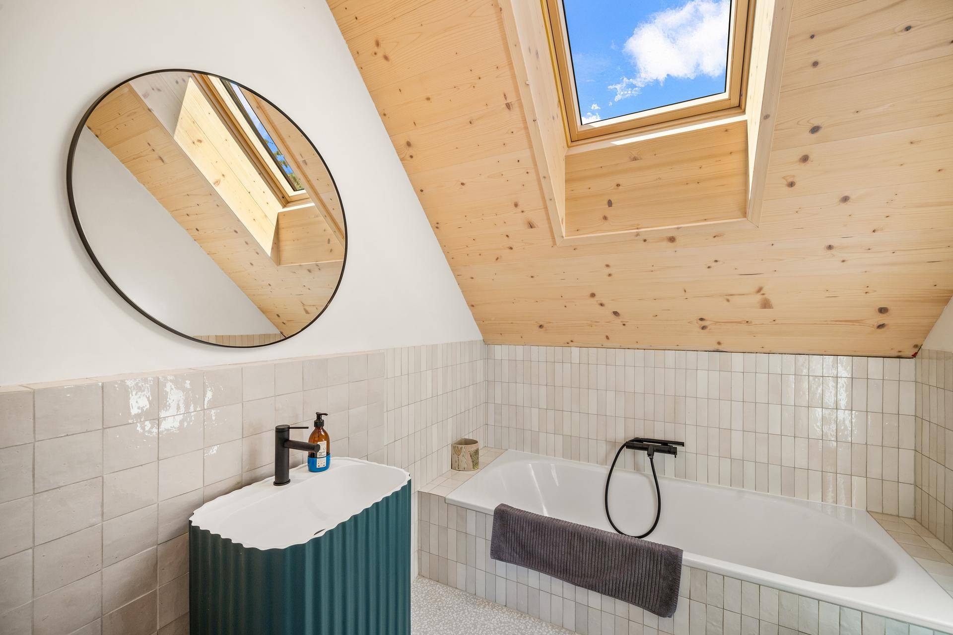 Dachbadezimmer mit Holzdecke, Dachfenster, Badewanne und modernem Waschtisch.