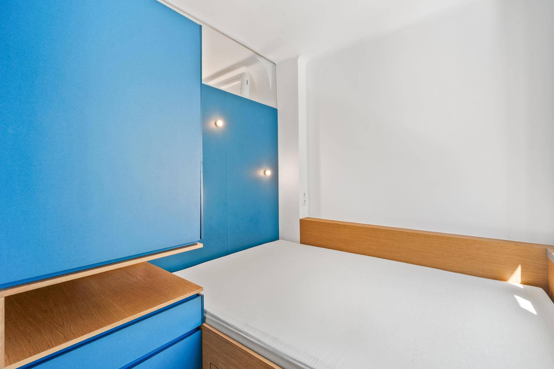 Gemütlicher Schlafbereich mit integriertem Bettrahmen und blauer Wandverkleidung für eine moderne Atmosphäre.