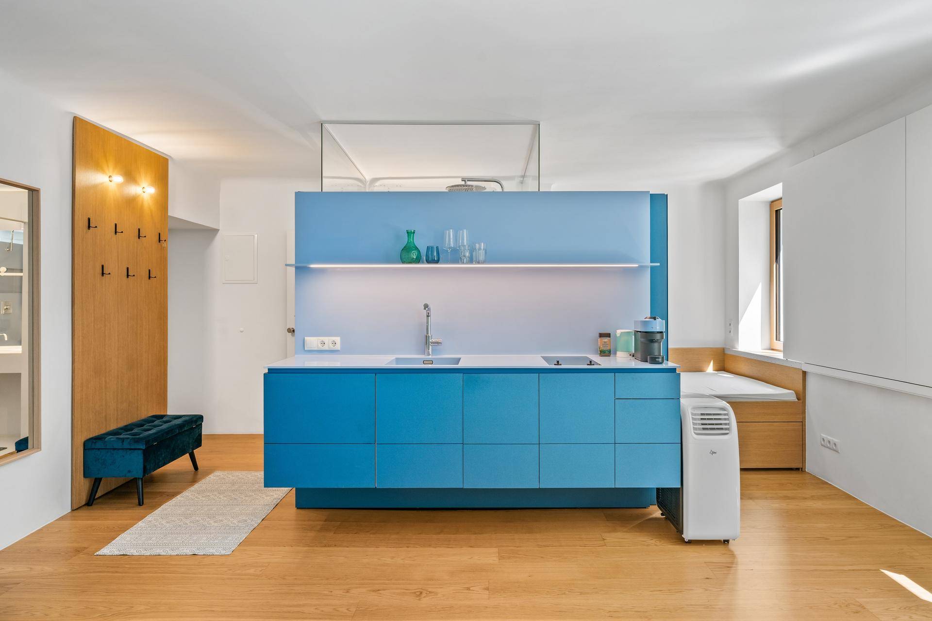 Moderne blaue Küchenzeile mit integrierter Beleuchtung und angrenzendem Schlafbereich in hellem Ambiente.