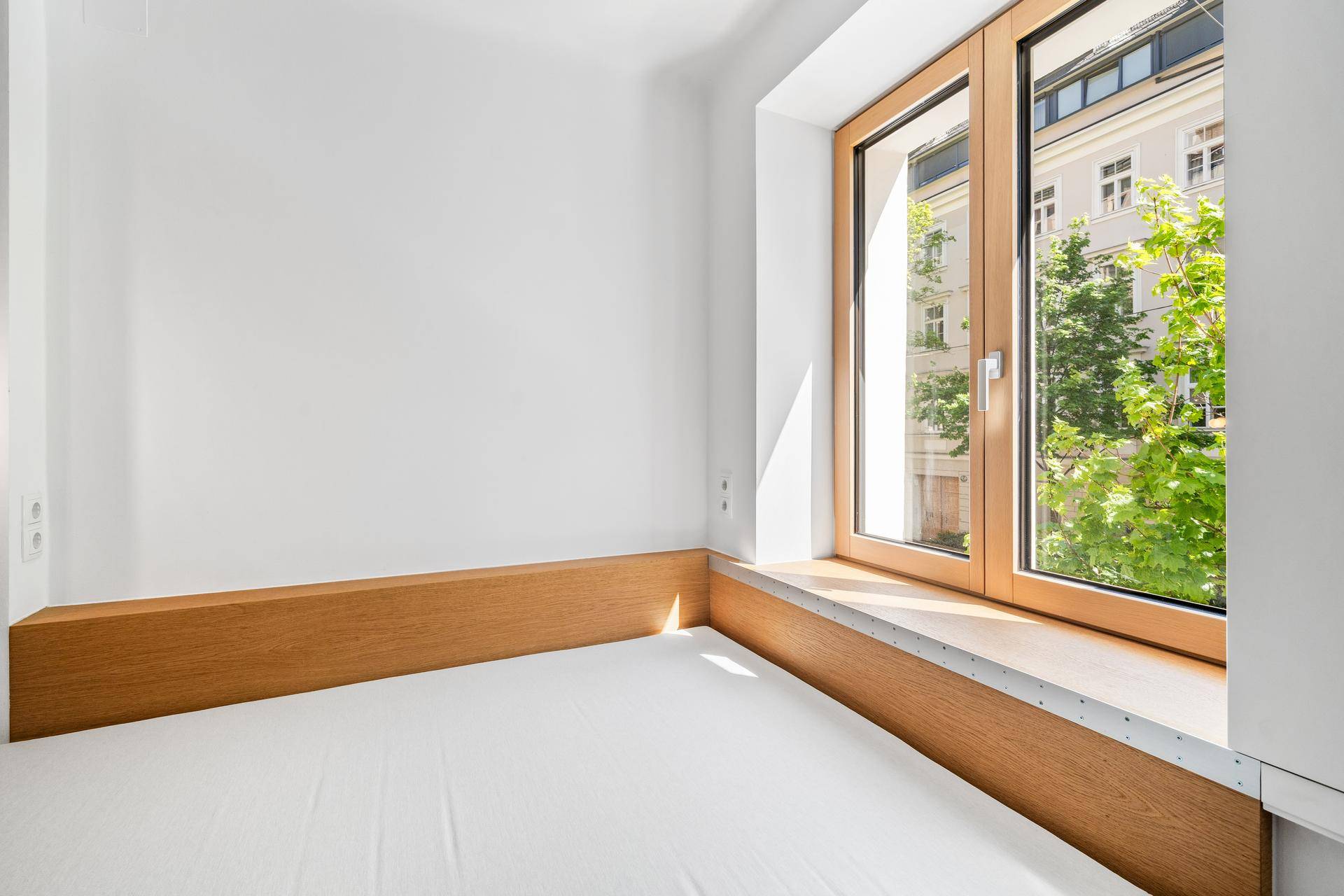Heller Schlafbereich mit großem Fenster, das viel Tageslicht und einen Blick ins Grüne bietet.
