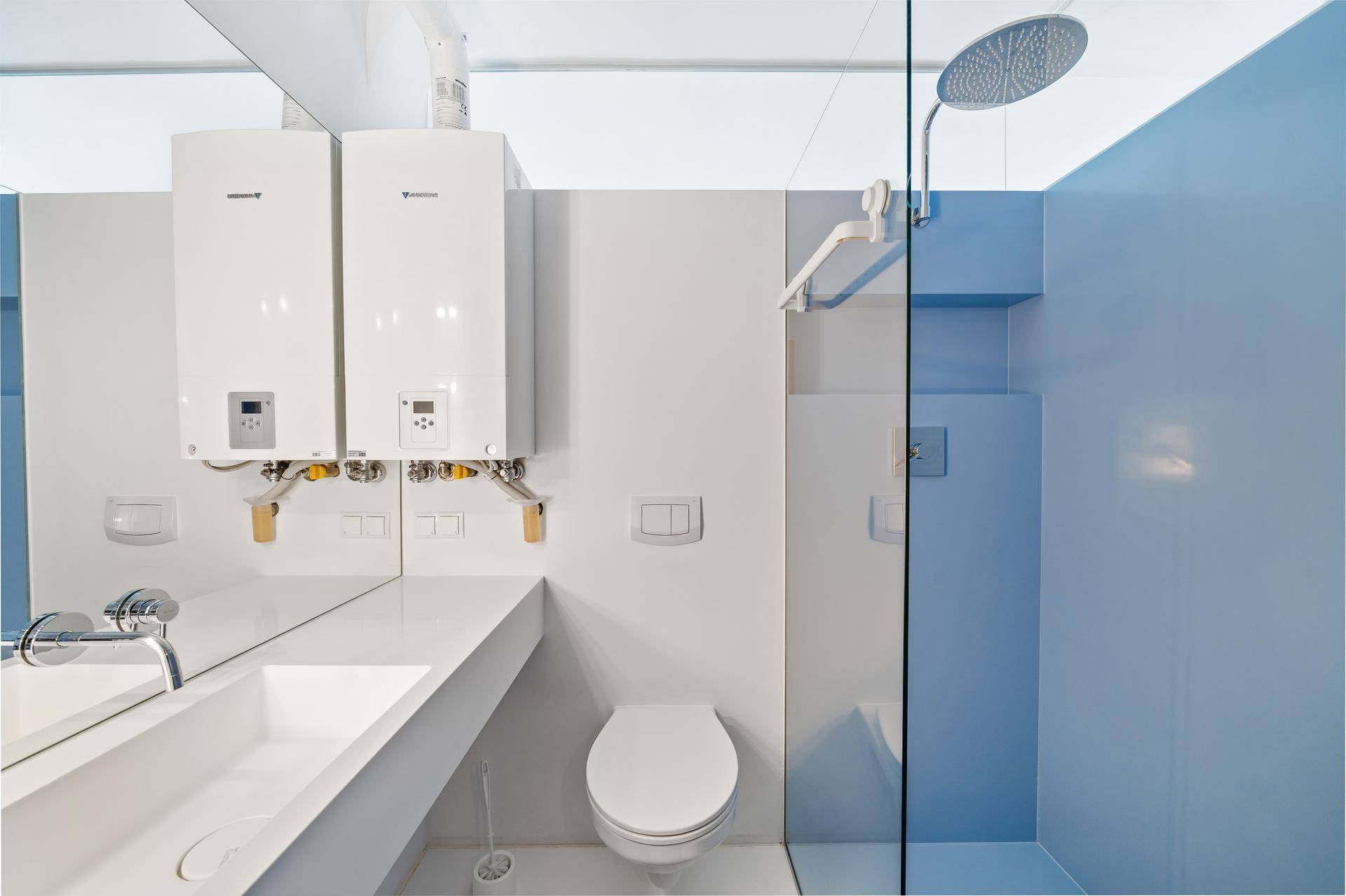 Modernes Badezimmer mit Dusche, Waschbecken, Toilette und zwei Warmwasserbereitern an der Wand.