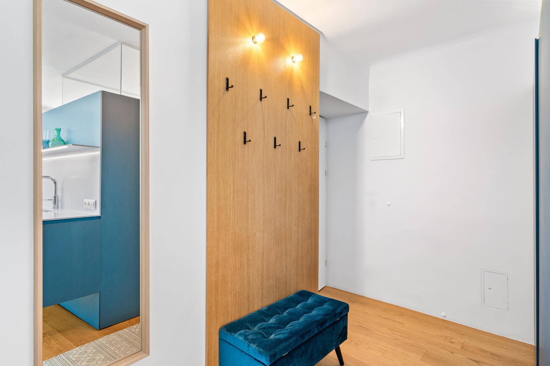 Eingangsbereich mit Holzwand, Garderobenhaken, großem Spiegel und einer blauen Samtbank.